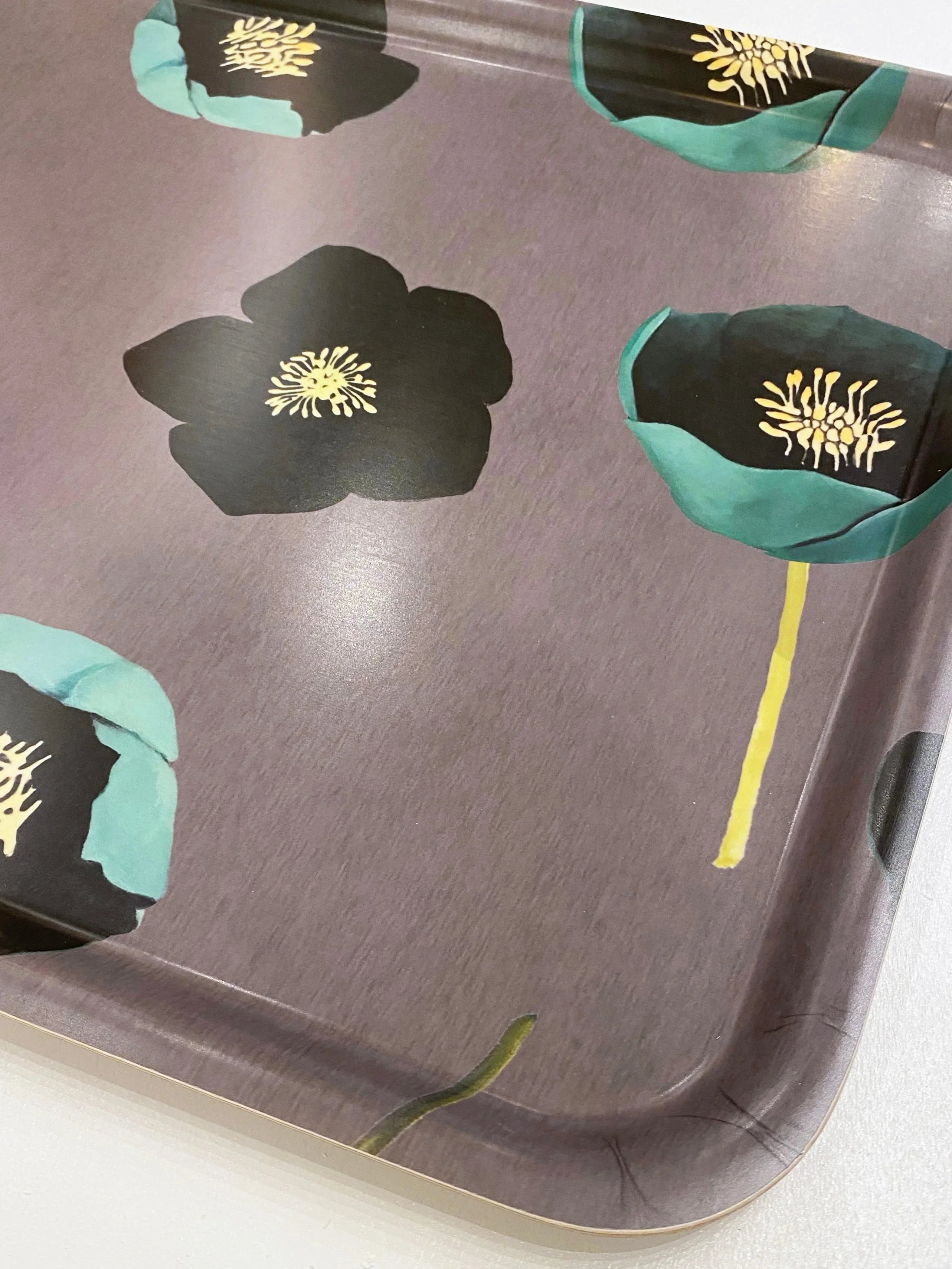 Close-up of a decorative tray with green and black winter rose flower design on a muted purple background