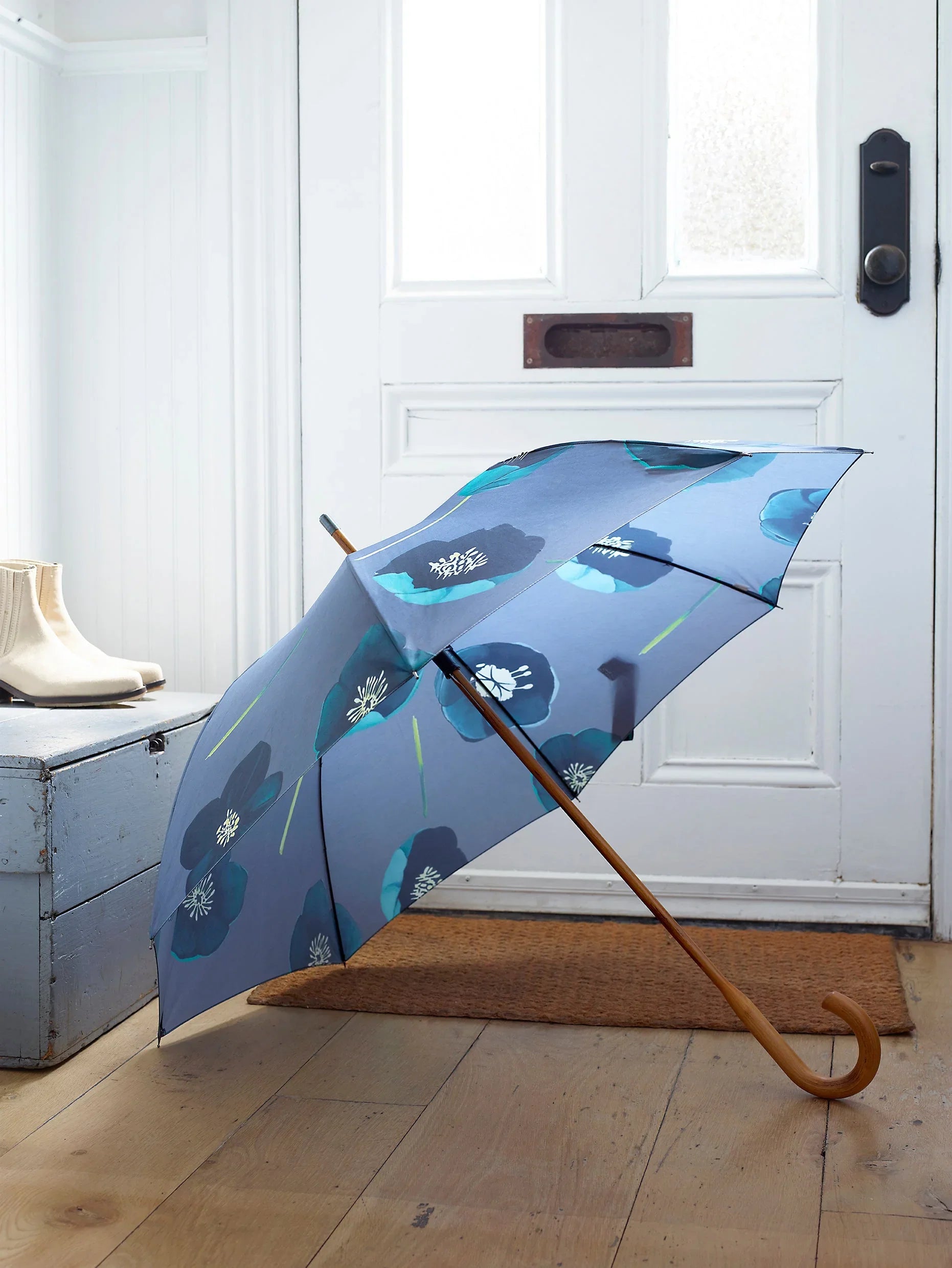 Blue umbrella with large floral print and wooden curved handle in bright entryway