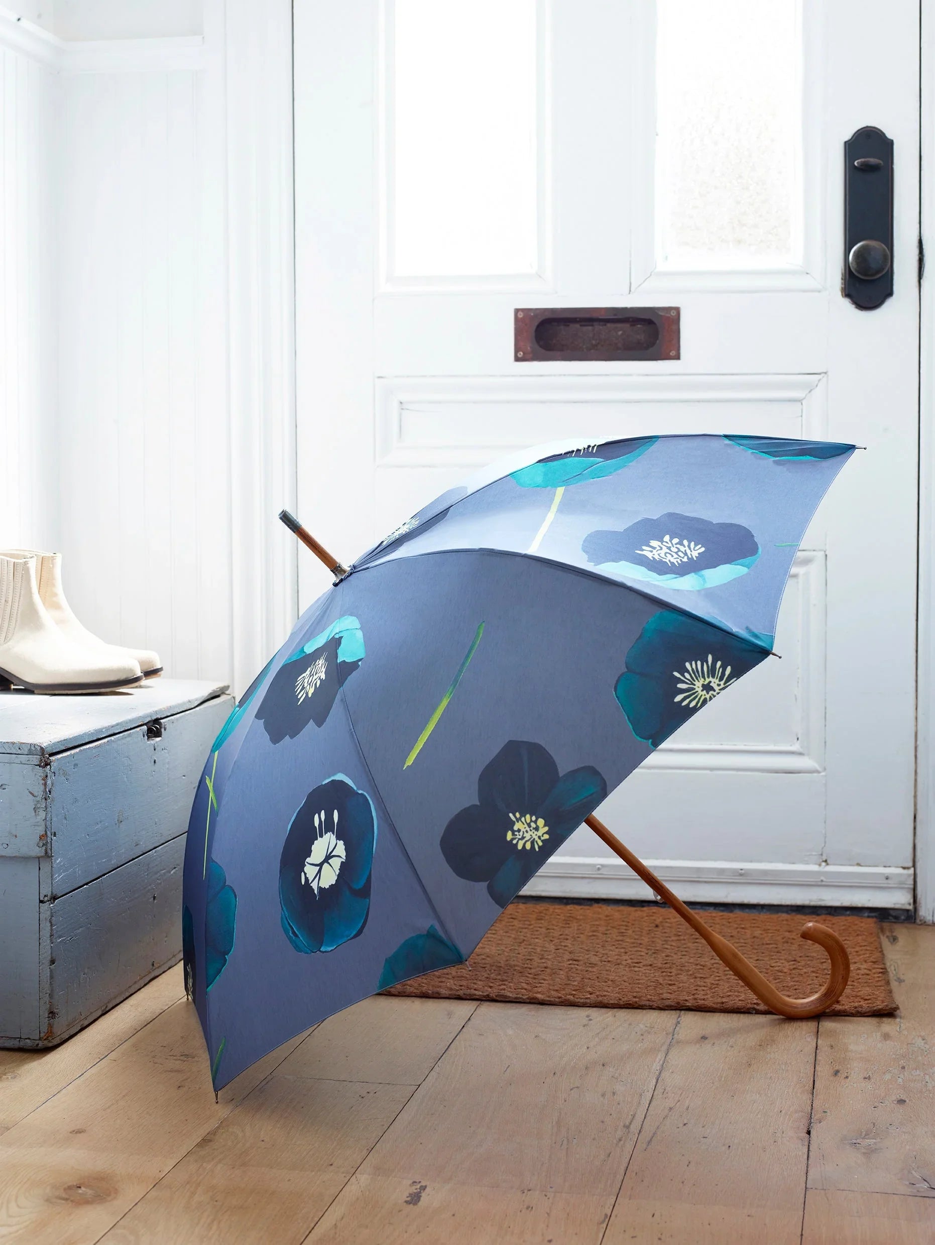 Blue umbrella with green and black winter rose flower pattern on wooden floor by white door