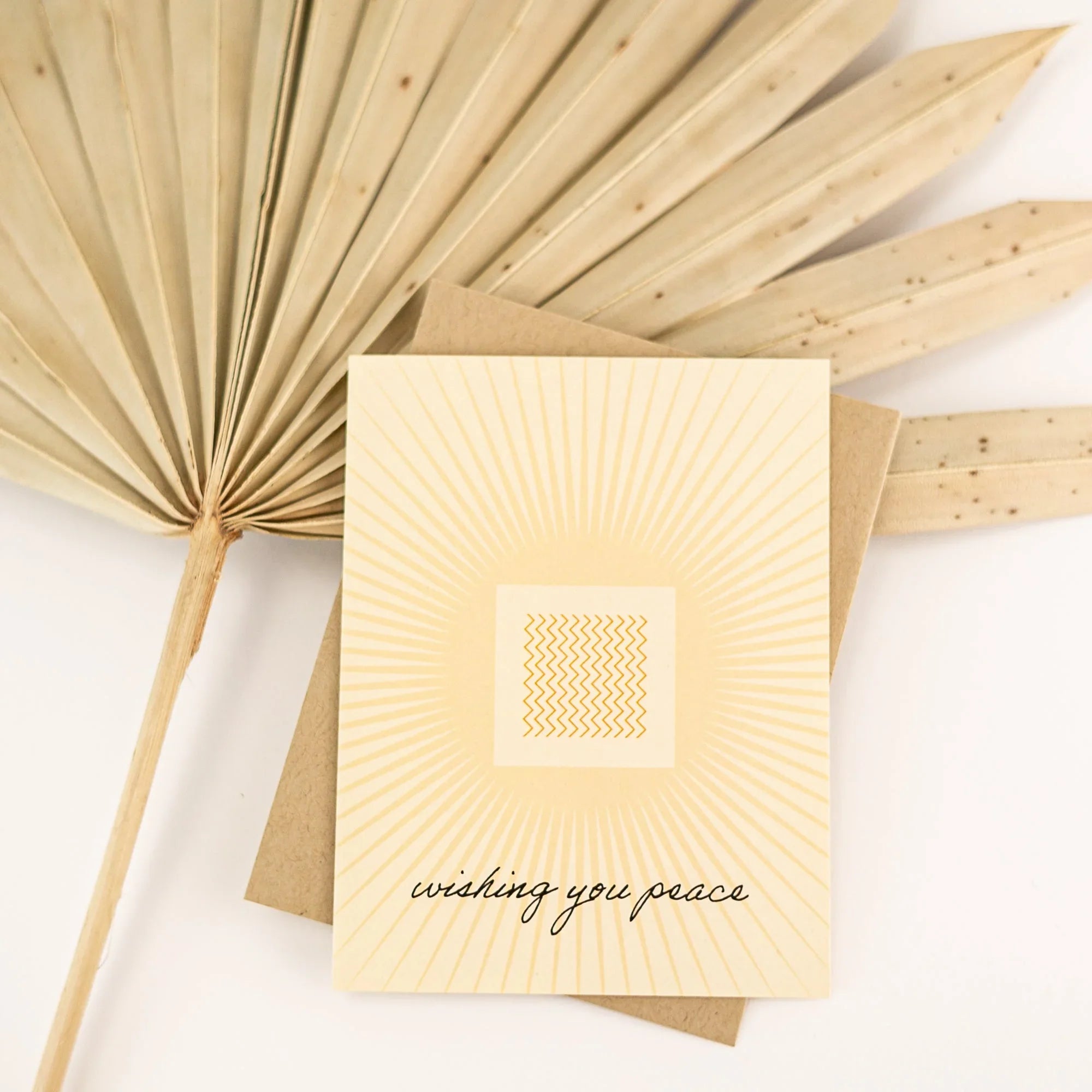 Minimalist greeting card with sunburst design and 'wishing you peace' text on beige background