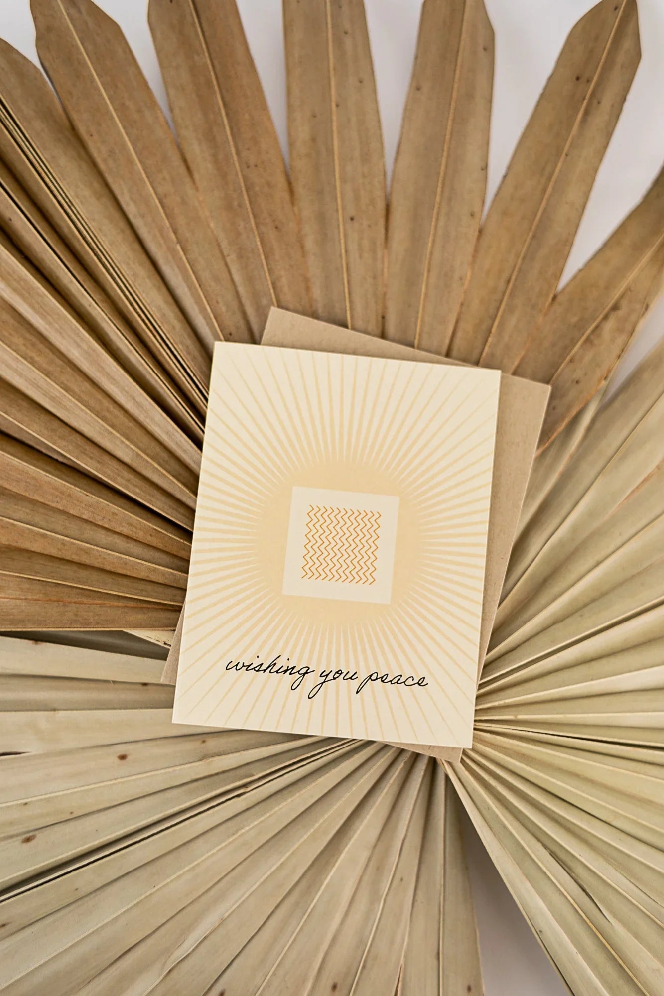 Minimalist greeting card with sunburst design and text 'wishing you peace' on dried palm leaves