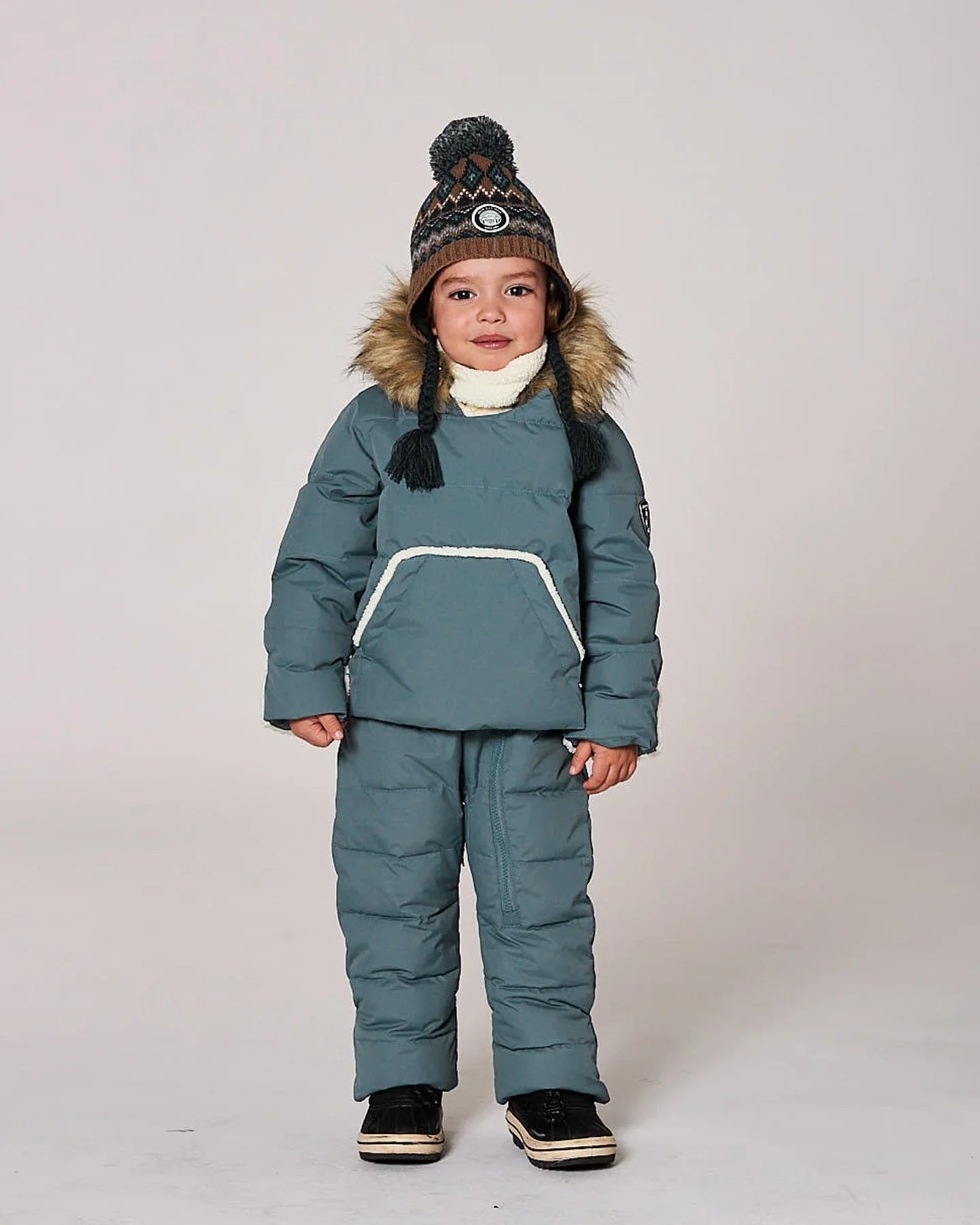 Child in blue winter snow suit with faux fur hood and knit hat, studio background, Qu!rk Boutique