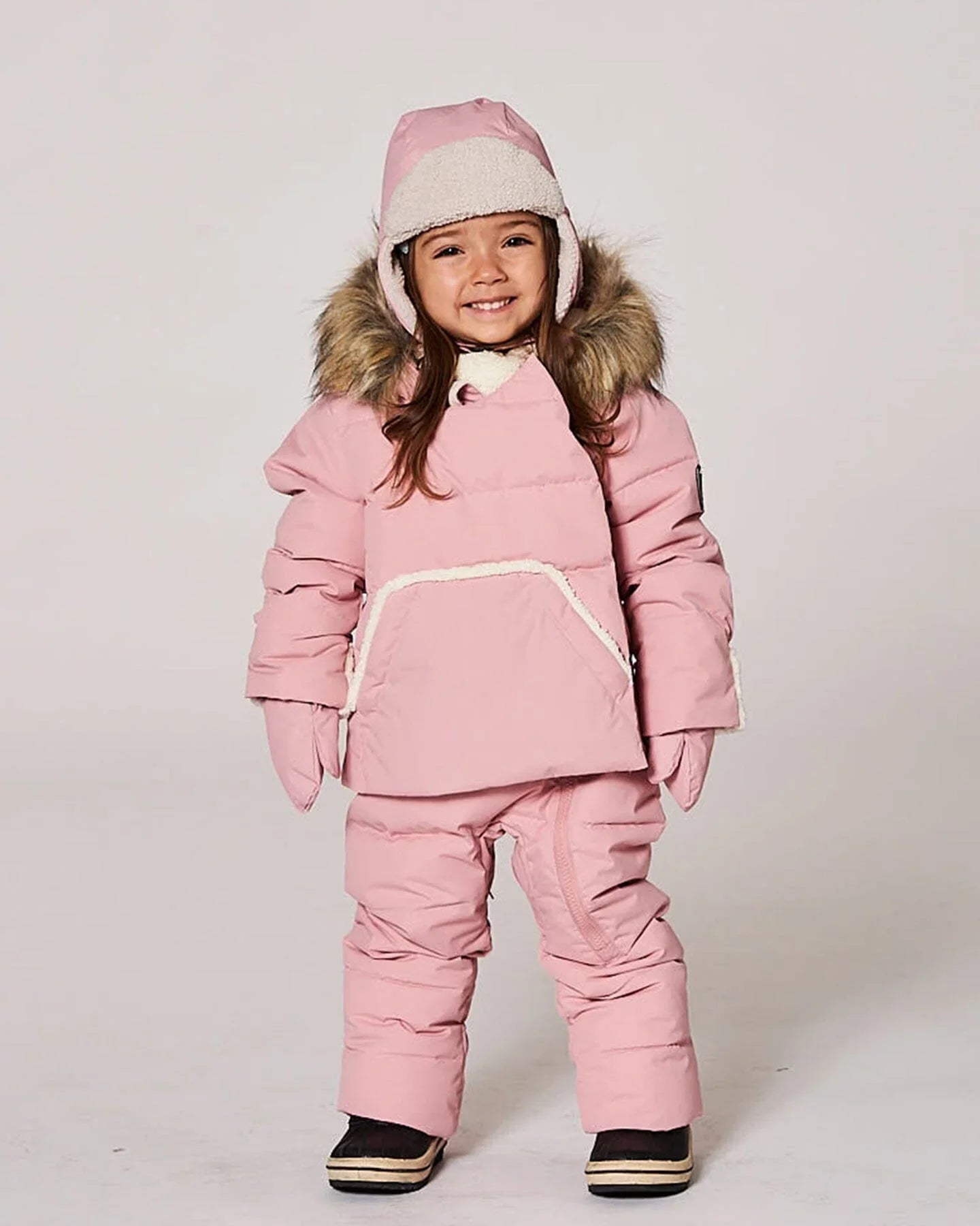 Smiling child in pink winter snowsuit, mittens, and faux fur hood at Qu!rk Boutique