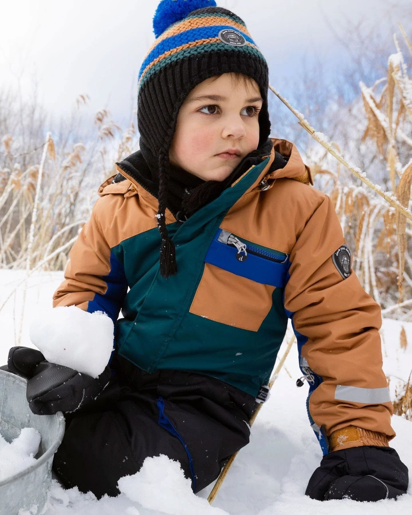 Child in colorblock winter jacket and knit hat playing in snow, Qu!rk Boutique winter wear