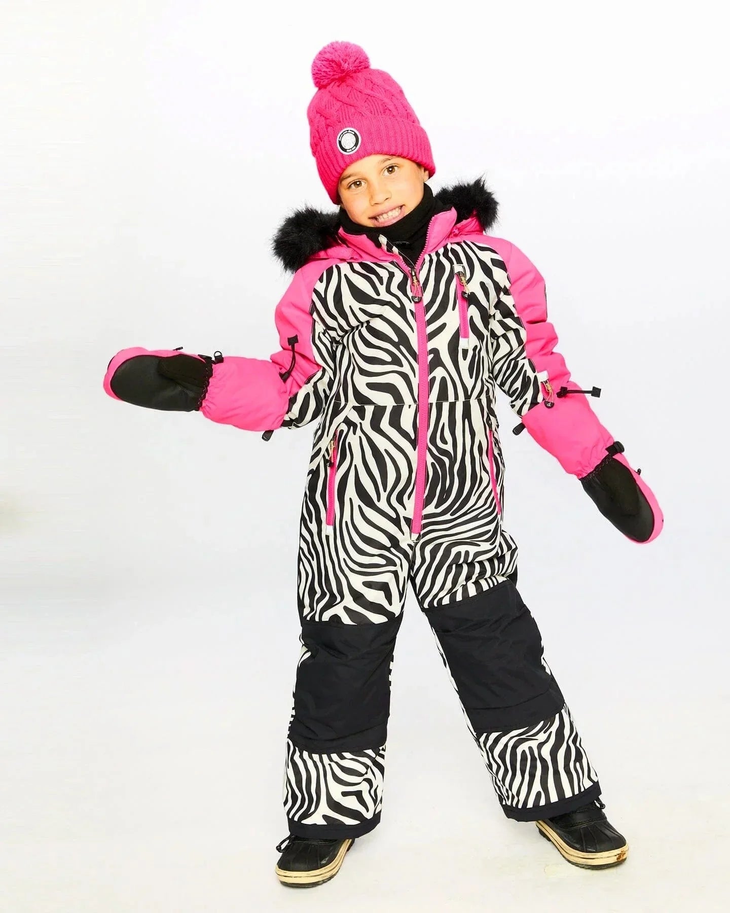 Smiling child in zebra-print snowsuit with hot pink accents and pom-pom beanie, winter fashion