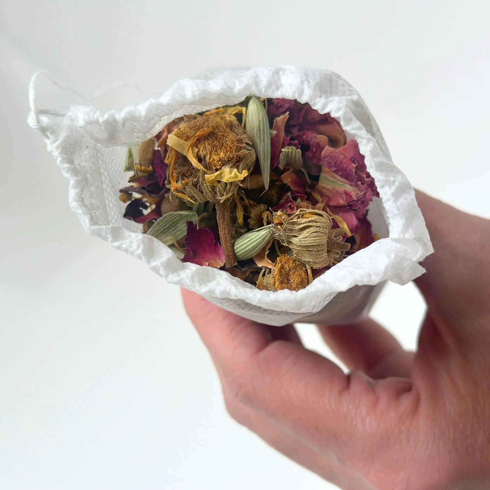 Hand holding a white tea bag filled with dried herbal bath tea with chamomile and rose petals