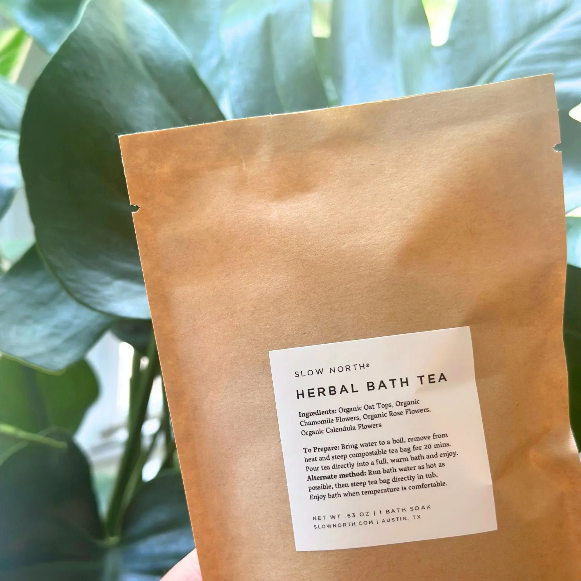 Slow North Herbal Bath Tea package with organic ingredients label held in front of green leaves