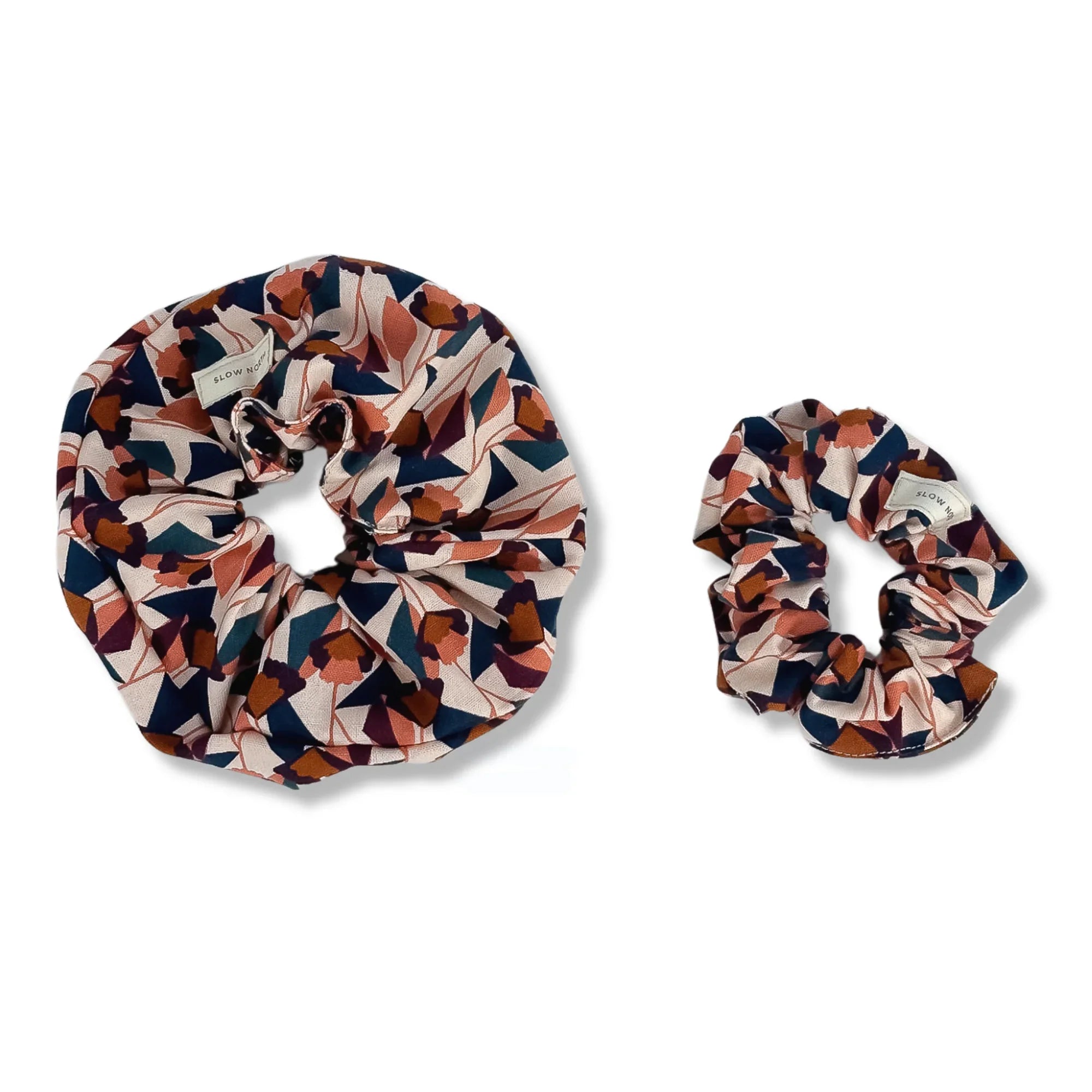 Two fabric hair scrunchies with geometric floral pattern in navy, rust, and beige colors on white background