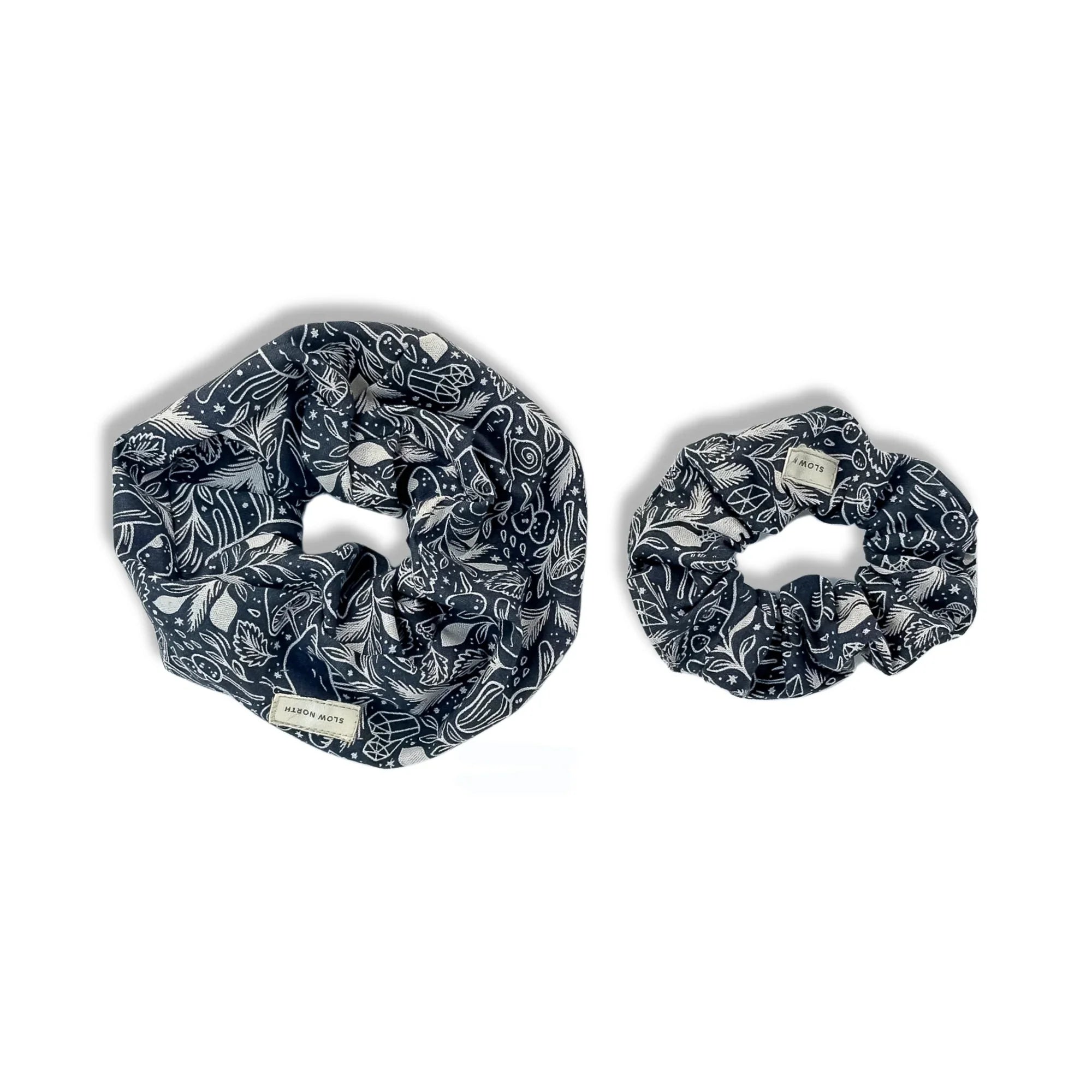 Two black fabric scrunchies with white botanical and geometric patterns on white background