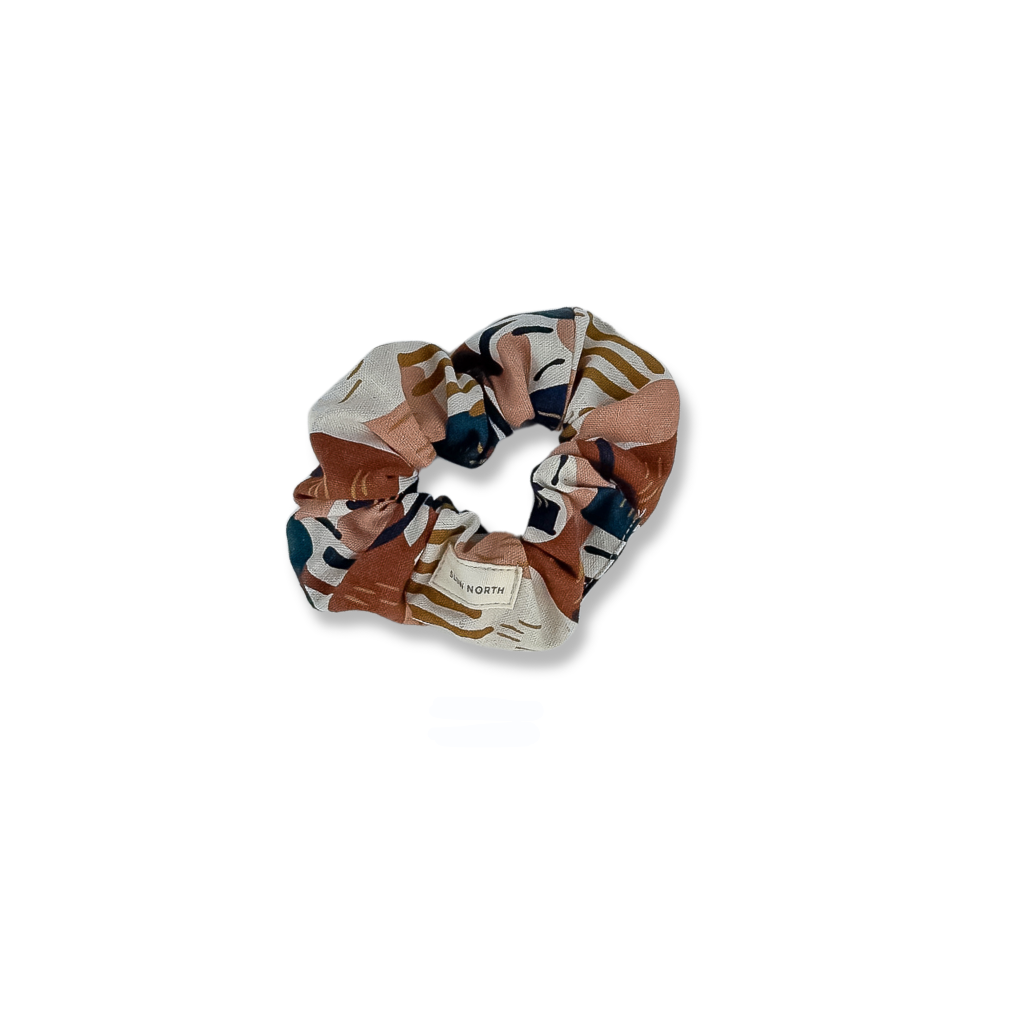 Abstract patterned fabric scrunchie with earth tones and a small label reading Down North