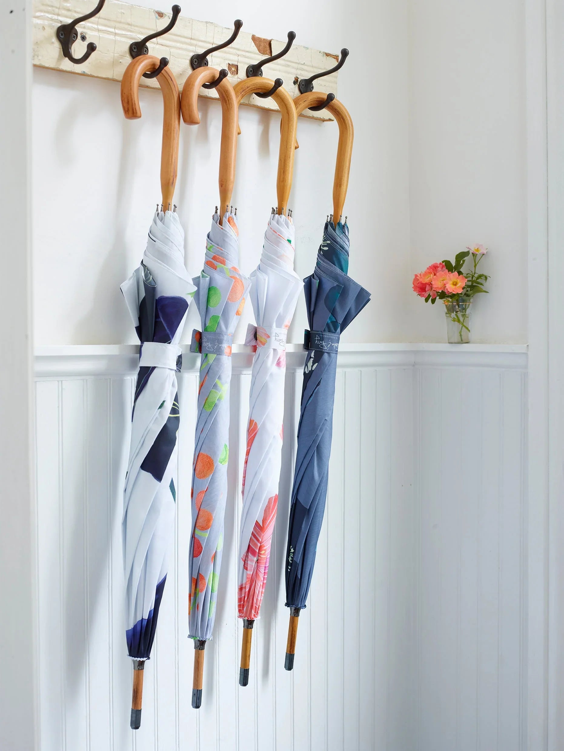 Four closed umbrellas with wooden handles hanging on wall hooks in white interior with flower vase
