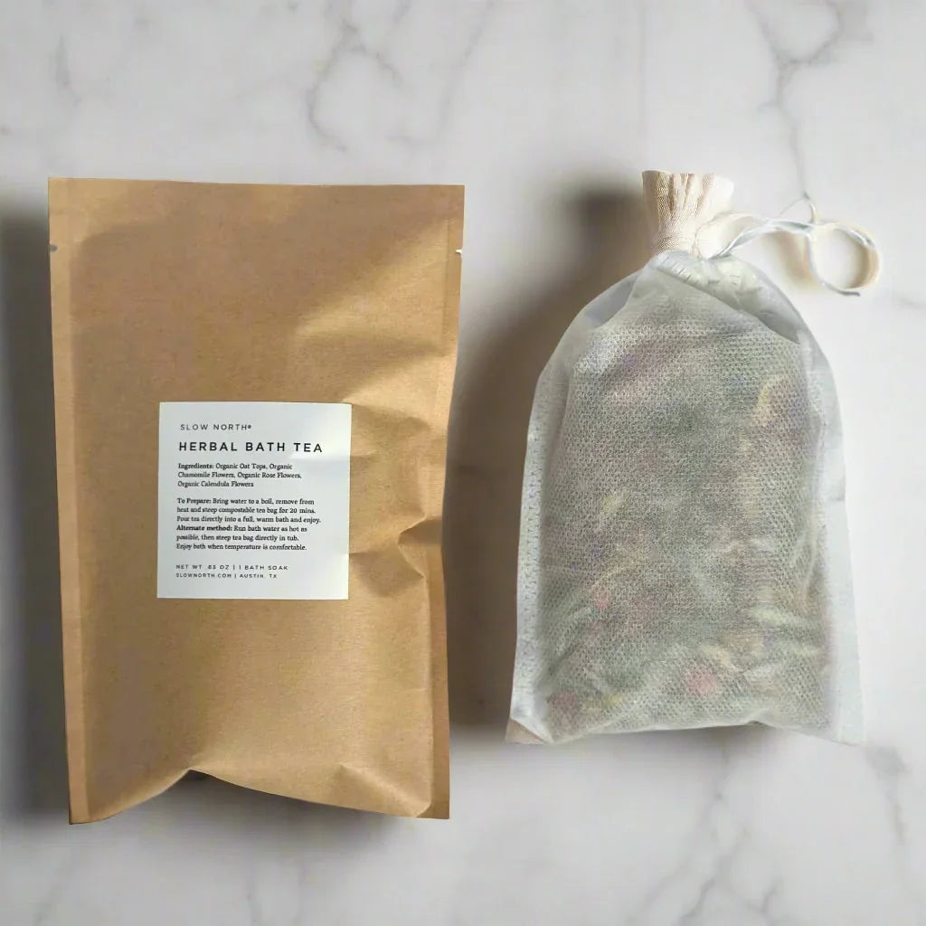 Slow North Herbal Bath Tea in kraft paper package with white label and mesh bath soak bag on marble surface
