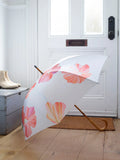 White umbrella with pink hibiscus flowers and curved wooden handle in a bright entryway