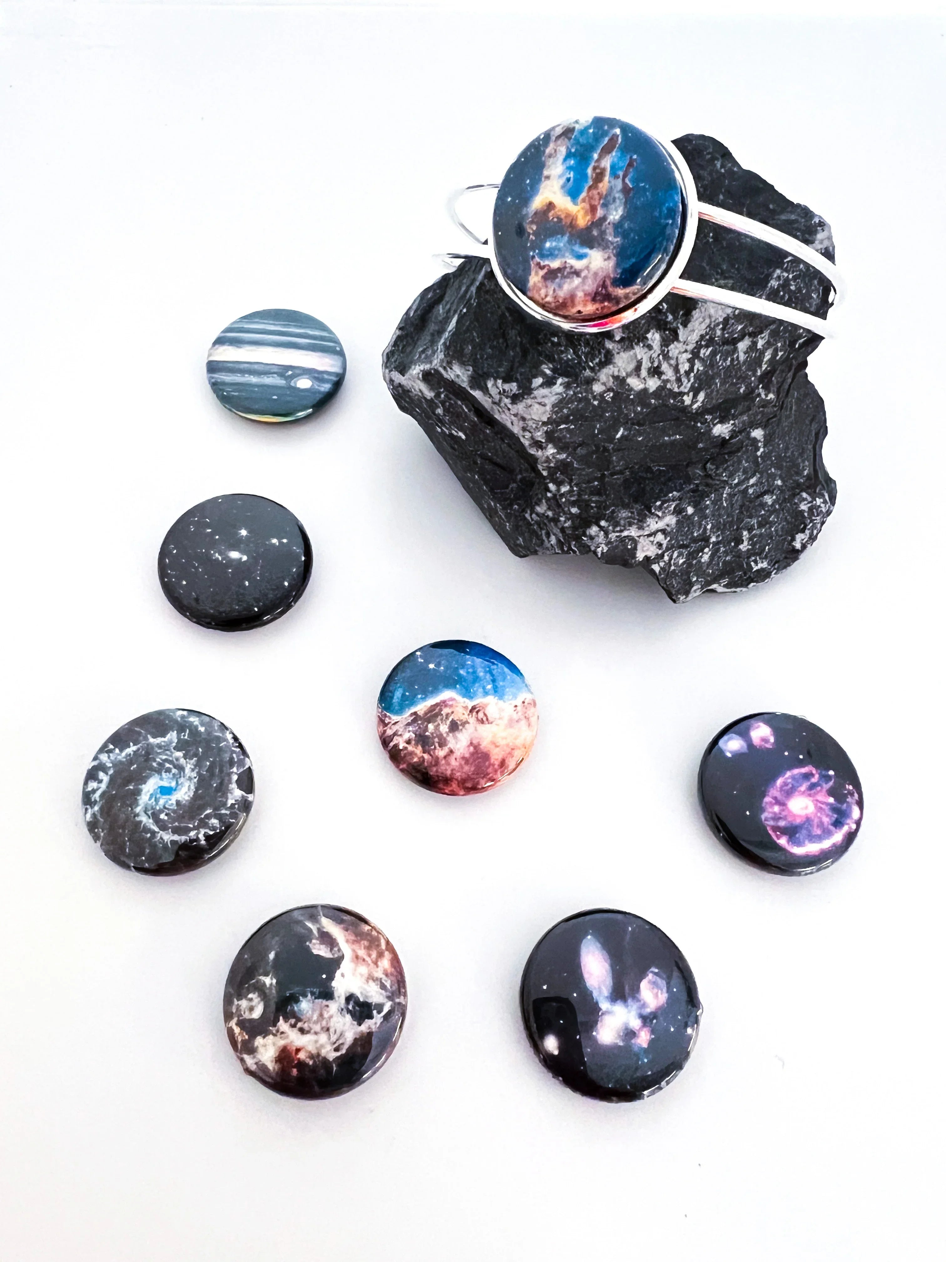 Galaxy-themed round pins and a bracelet with cosmic designs on a black rock, white background