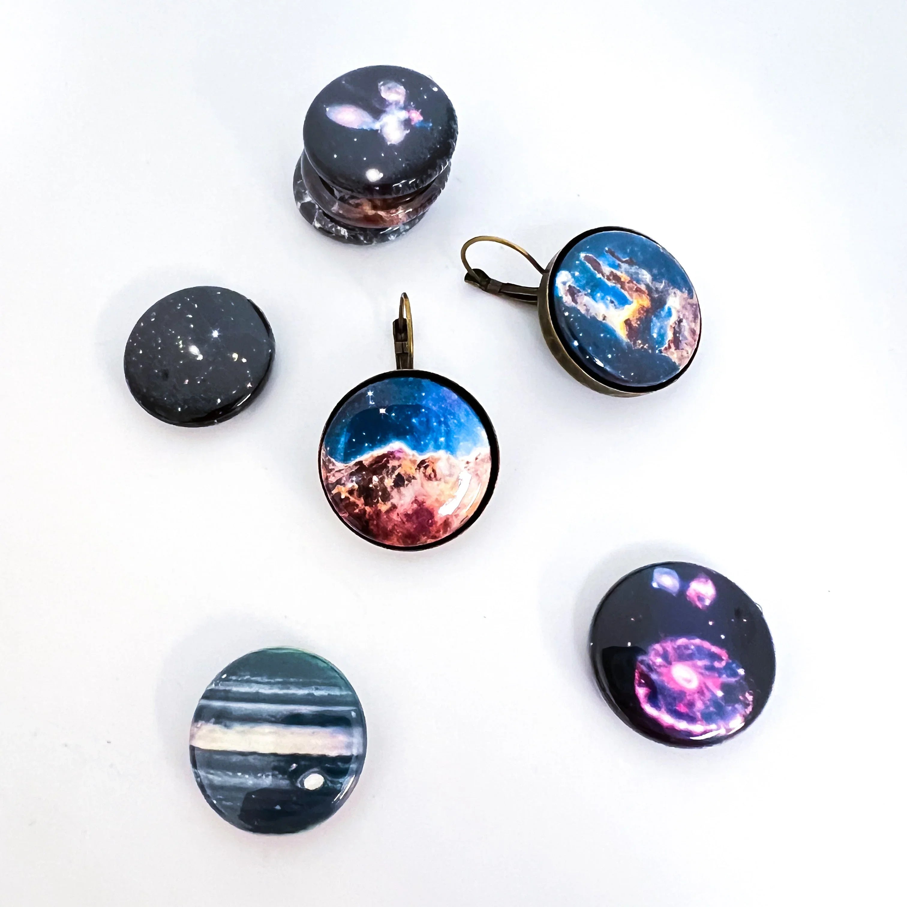 Round space-themed glass cabochons and earrings with galaxy and nebula designs on white background