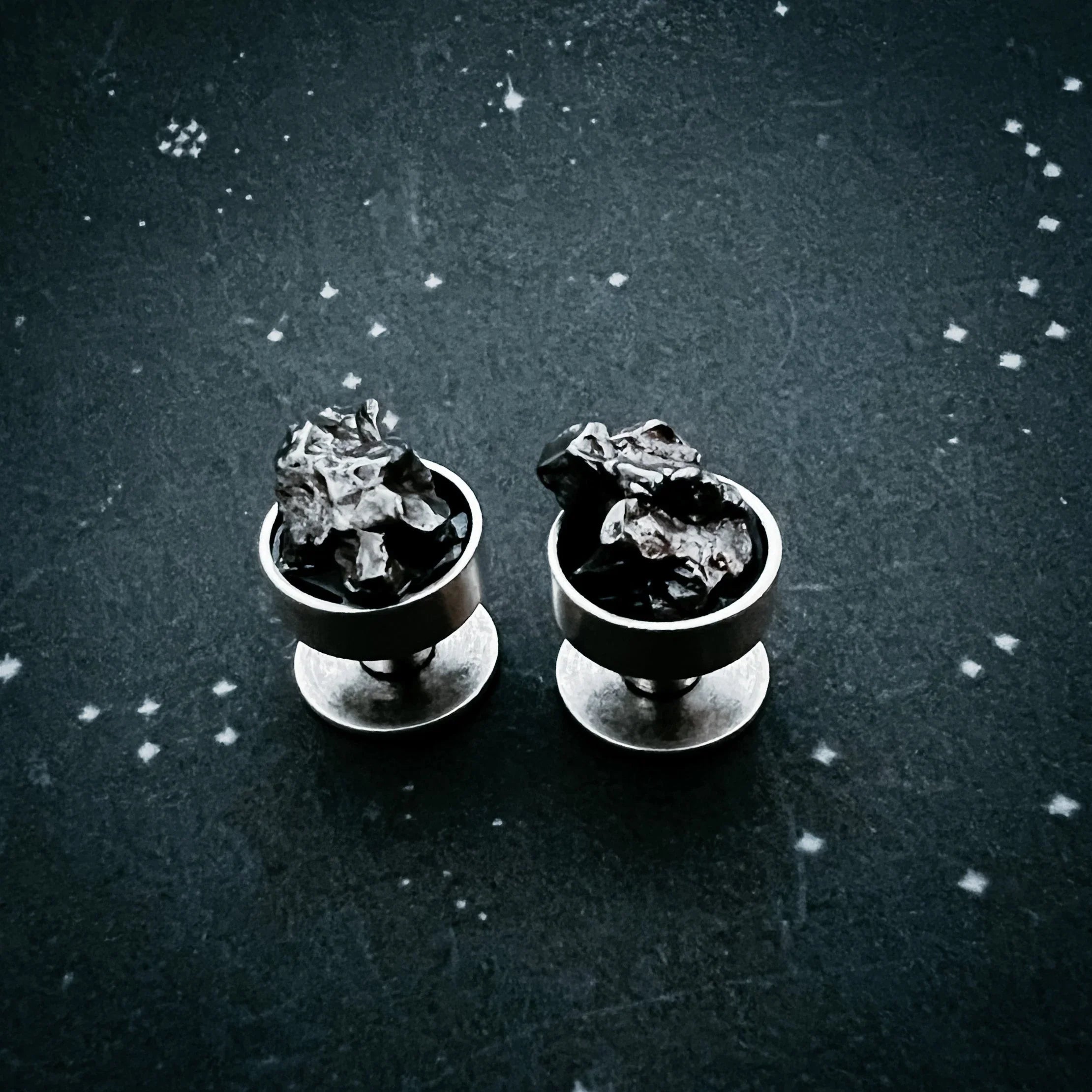 silver stud earrings with crumpled black metallic design on dark textured surface