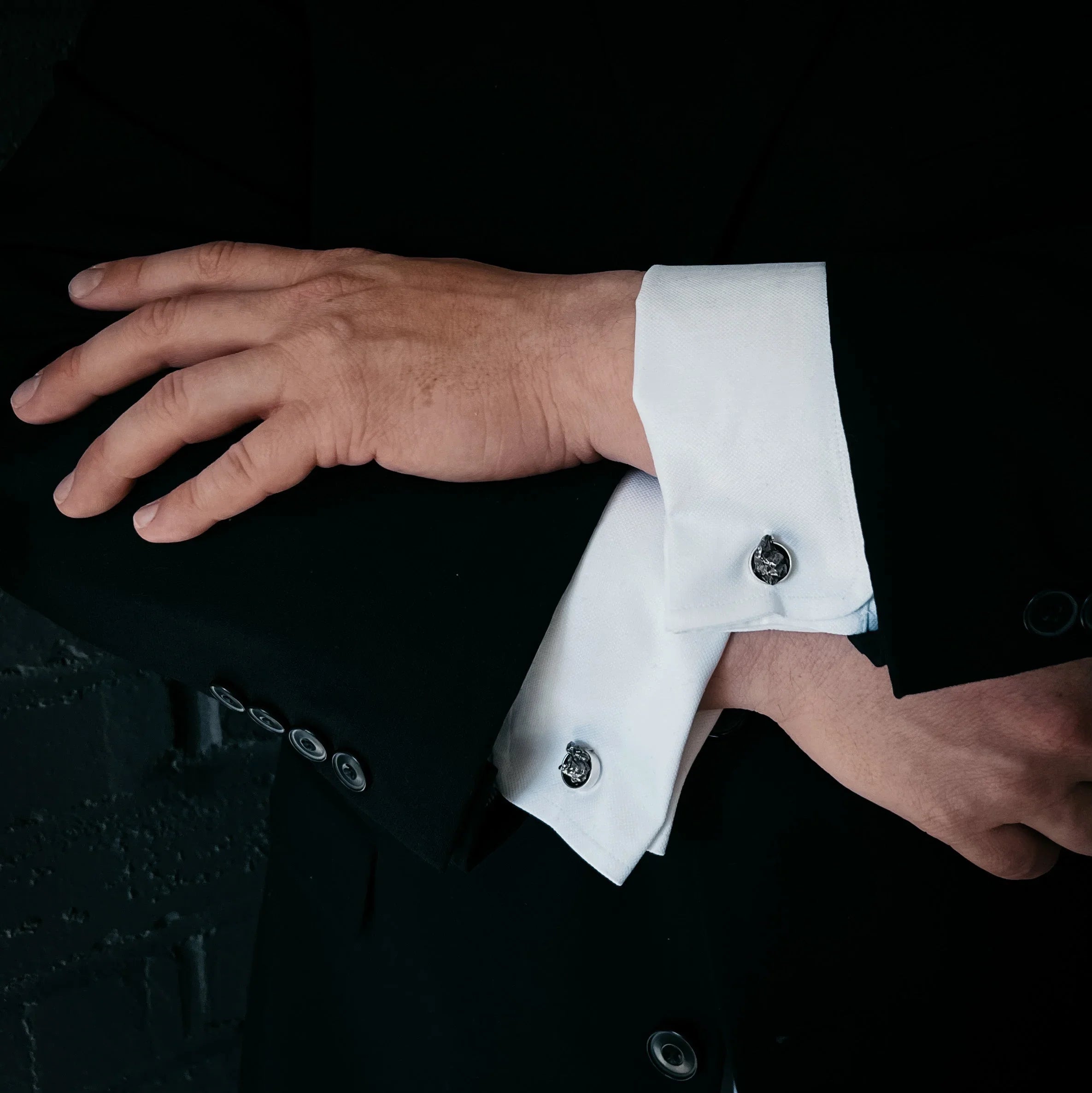 Close-up of man's arms crossed, wearing black suit with white French cuffs and silver cufflinks