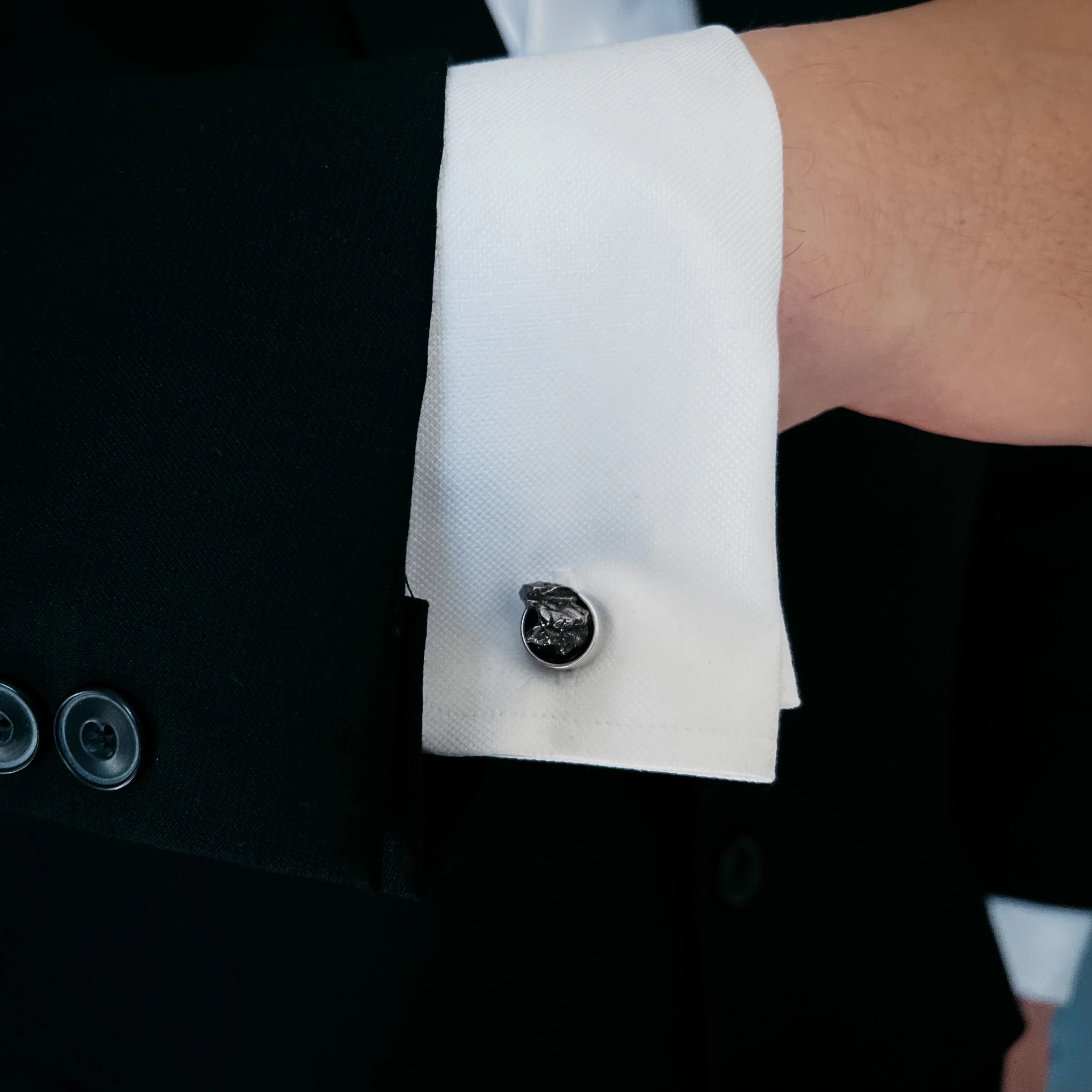 Close-up of a white dress shirt cuff with a silver cufflink worn under a black suit jacket sleeve