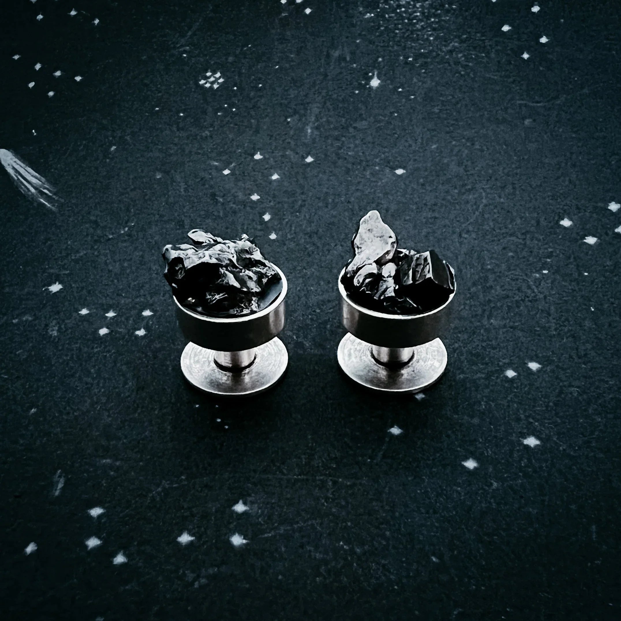 Pair of silver stud earrings with irregular black stones on a dark star-patterned surface