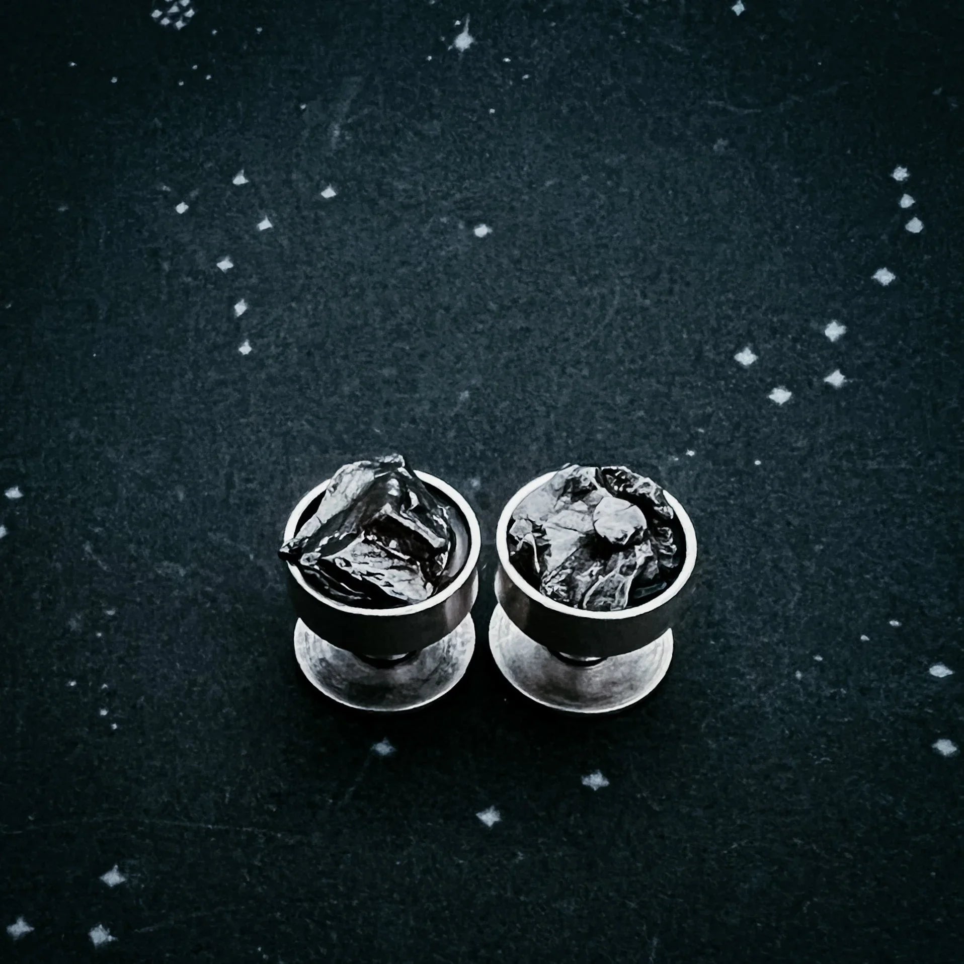 Pair of silver stud earrings with rough black stone on dark textured surface