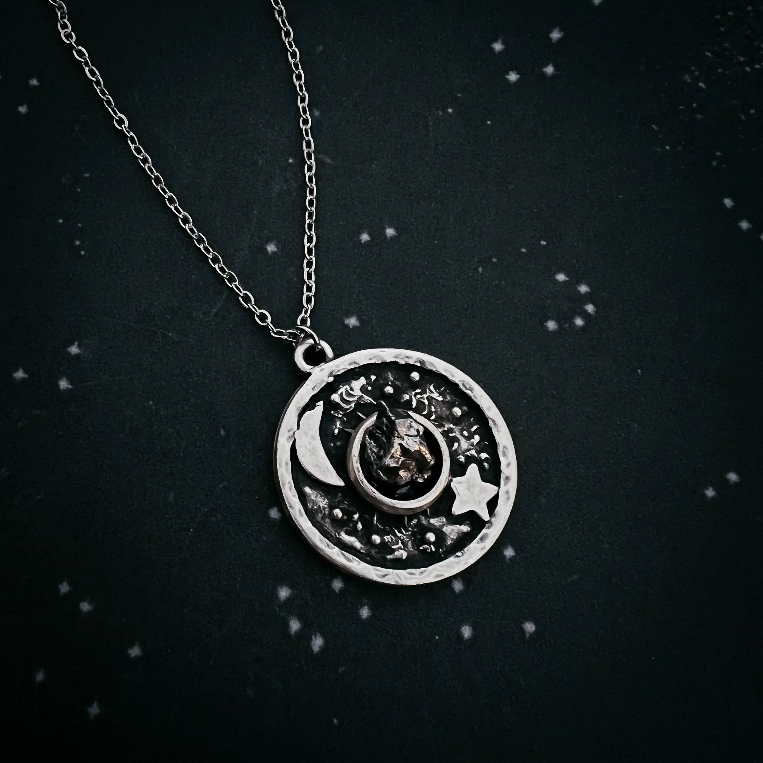 Silver pendant necklace with moon, star, and textured celestial design on dark background