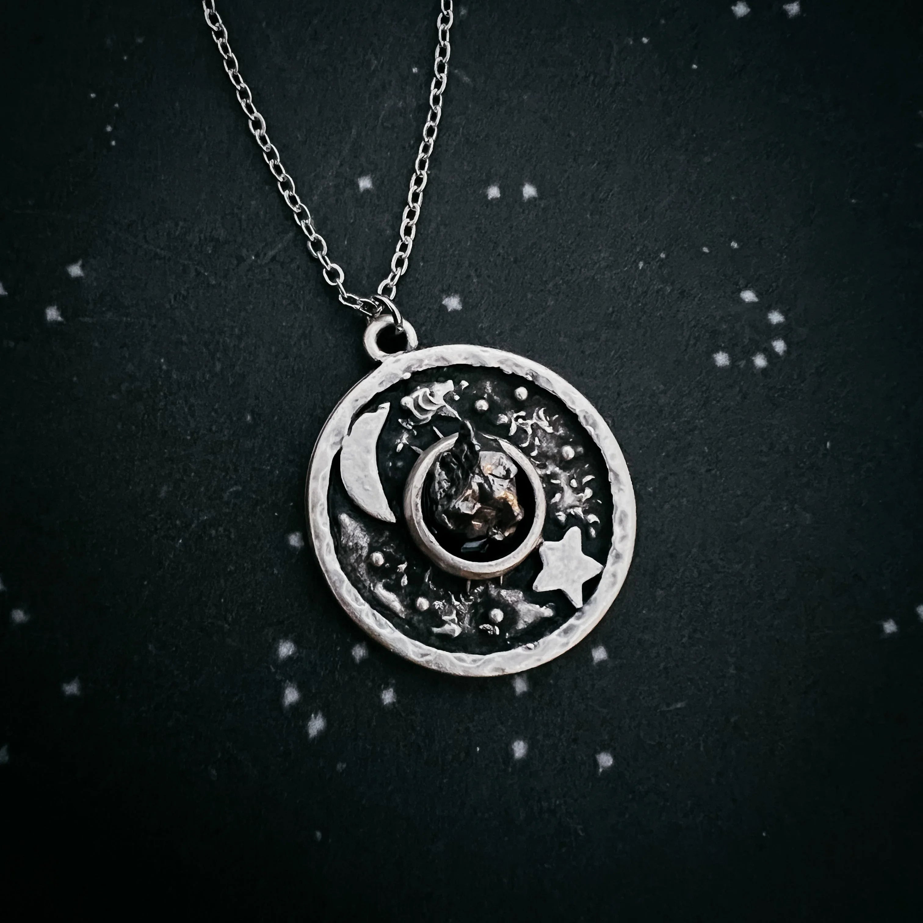 Silver celestial pendant necklace with crescent moon, star, and textured details on black background