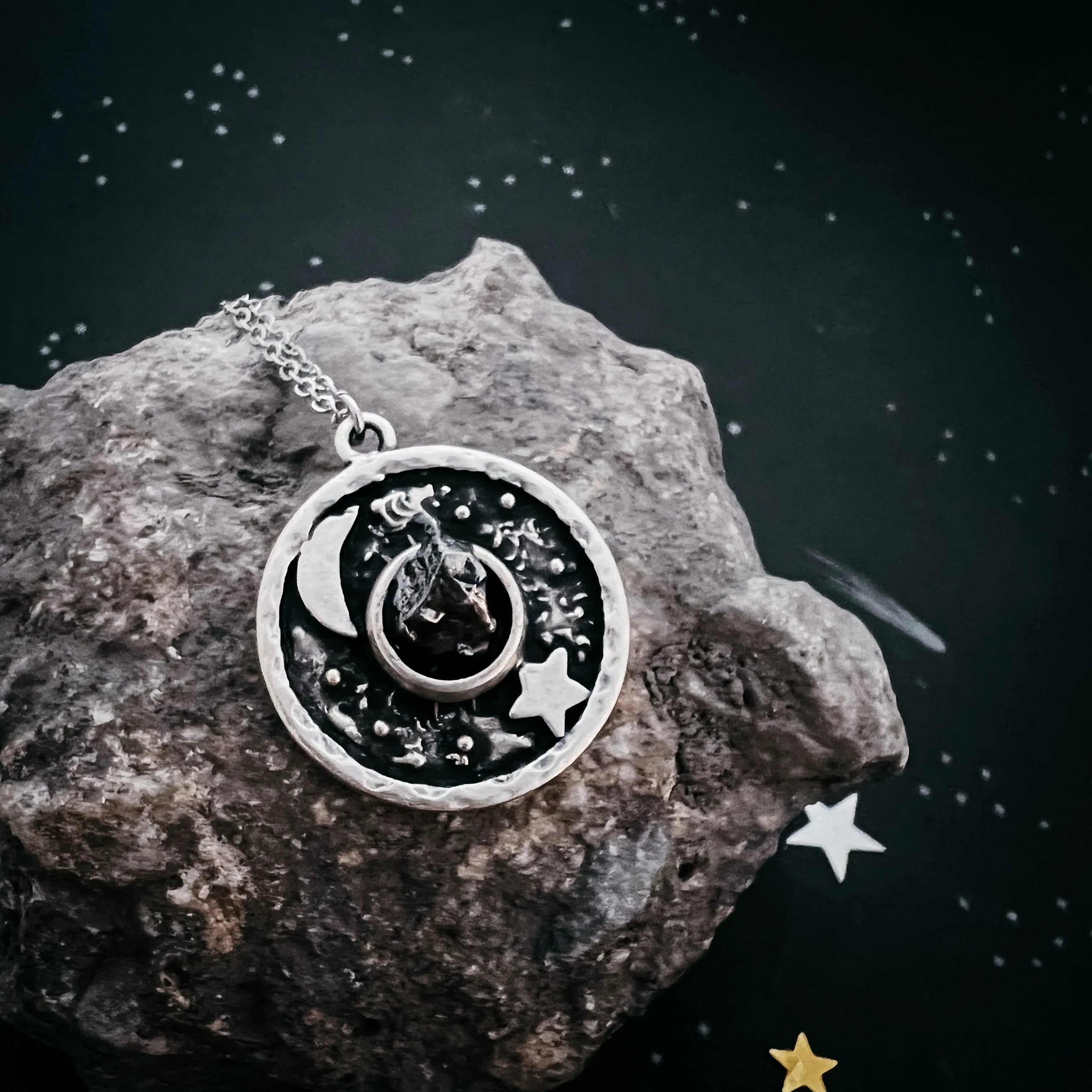 Silver lunar and star pendant necklace on textured rock with celestial background