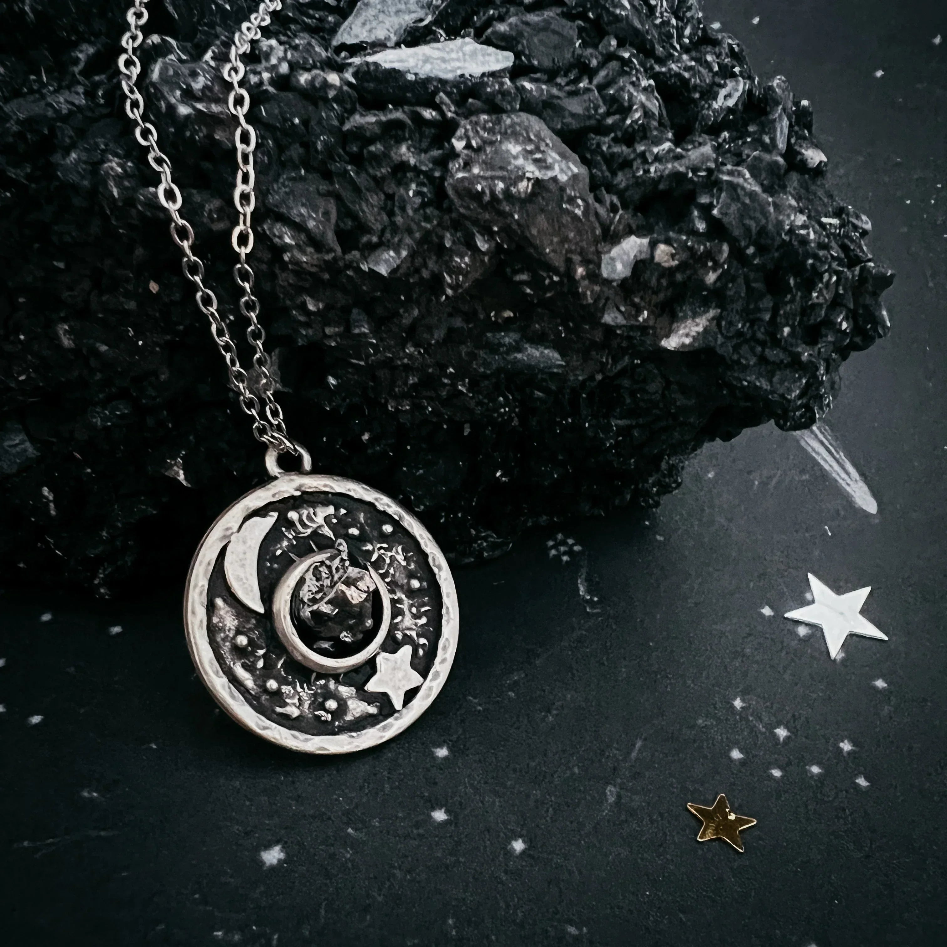 Silver moon and star pendant necklace on black textured surface with decorative star confetti