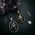 Cosmic teardrop galaxy necklaces on dark starry background with crystal, Qu!rk Boutique jewelry