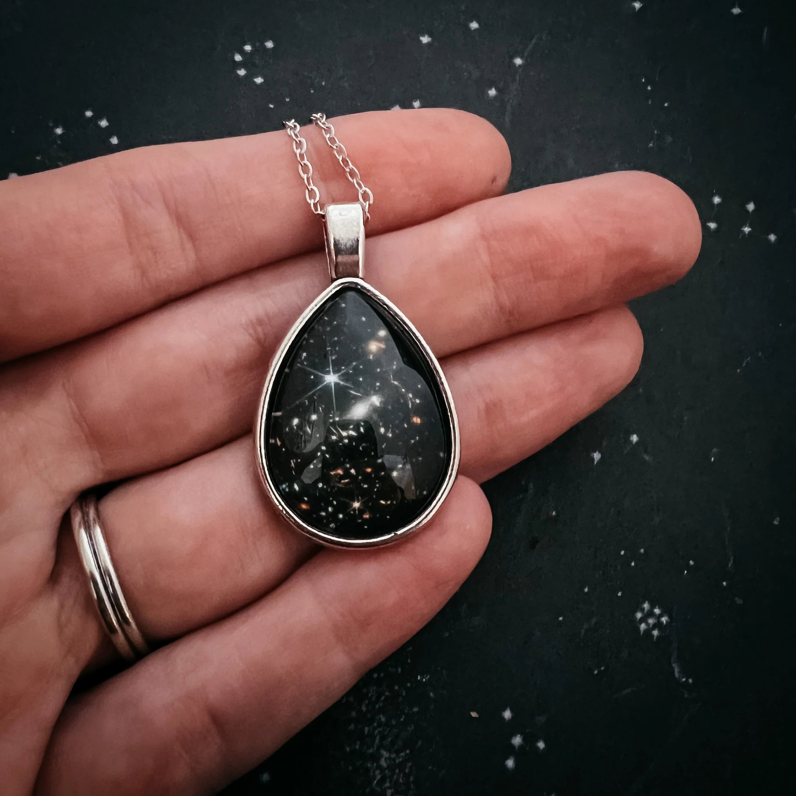 Cosmic teardrop galaxy pendant necklace on hand, artist-designed at Qu!rk Boutique