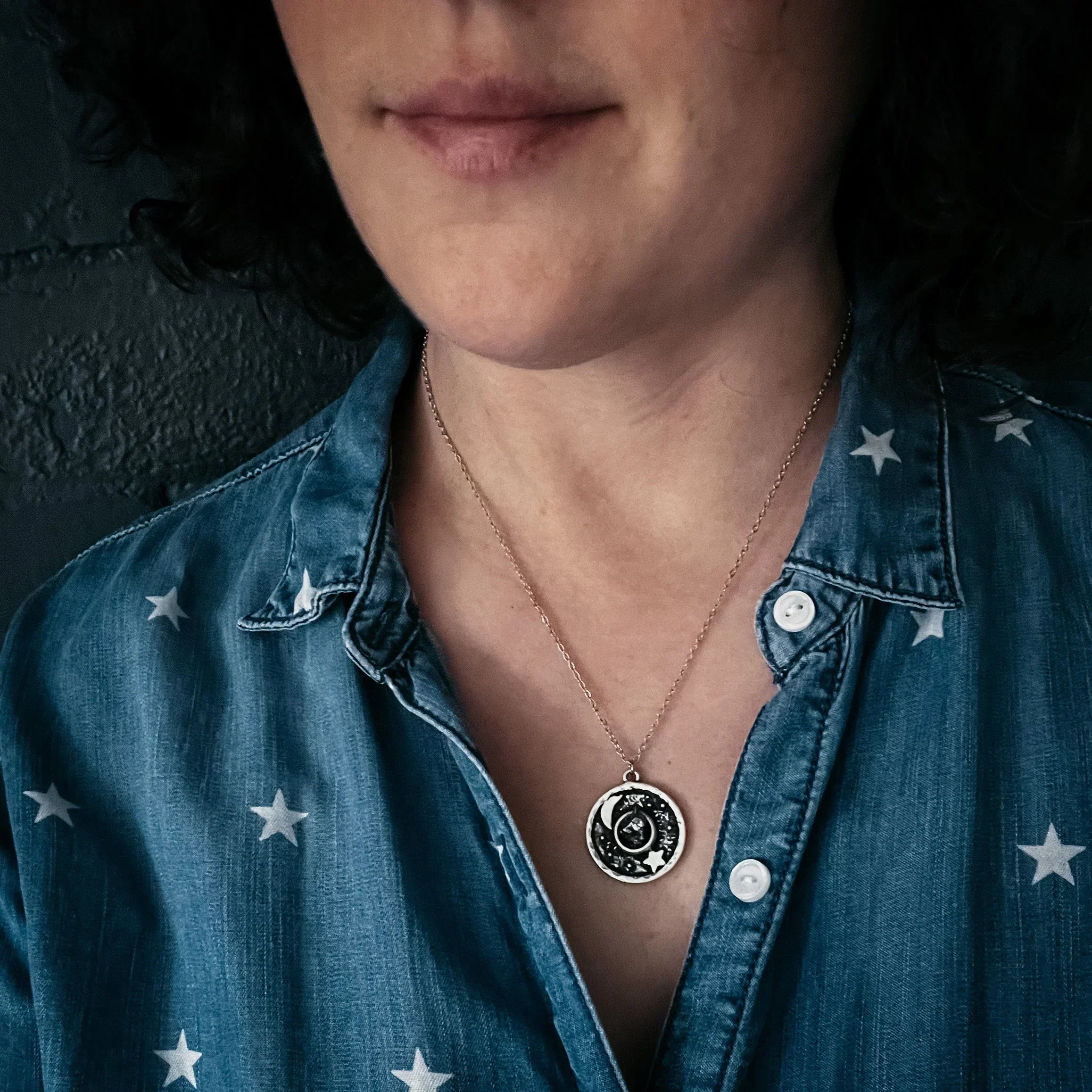 Close-up of a woman wearing a silver moon and star pendant necklace with a blue star-patterned denim shirt