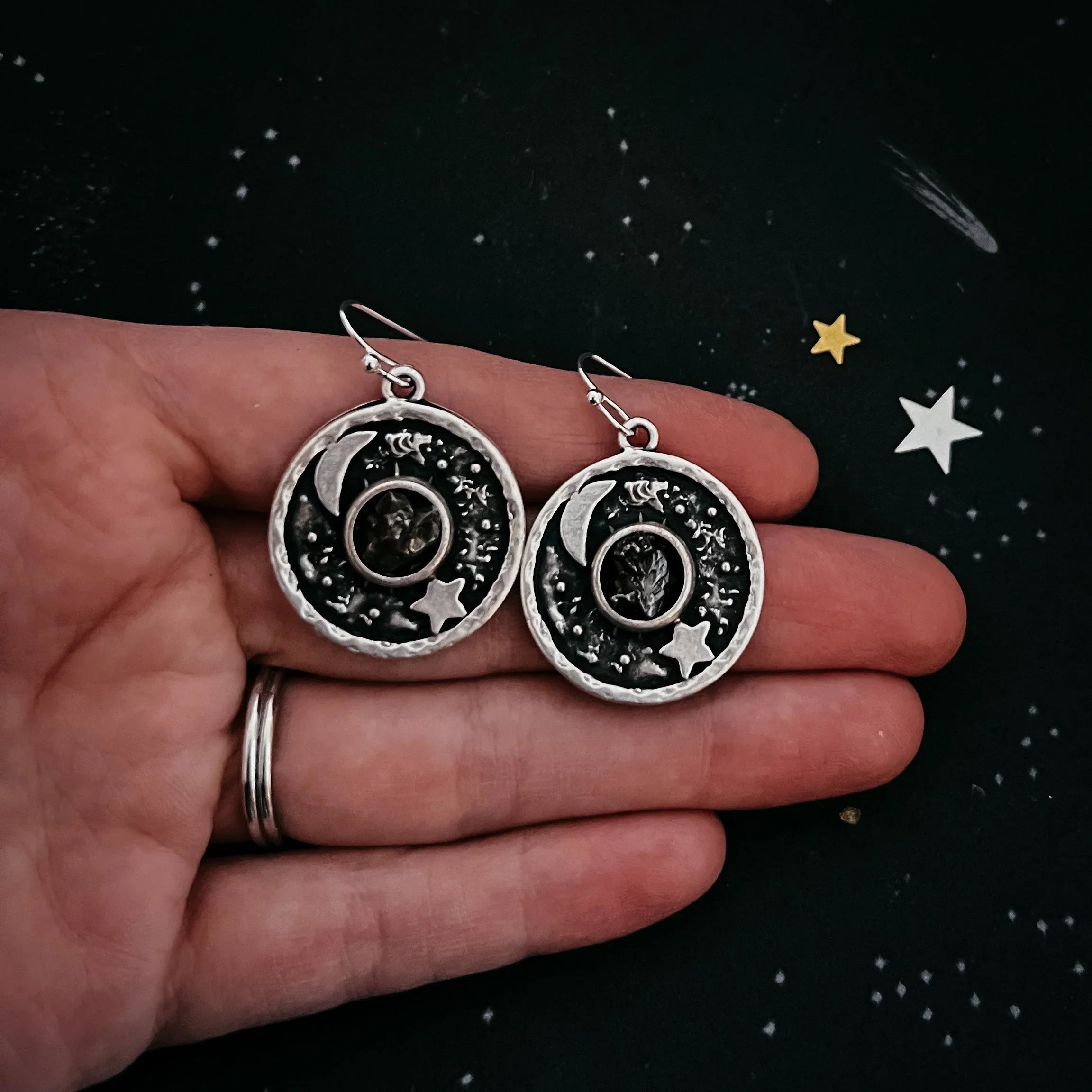 Hand holding round cosmic-themed earrings with moon and star from Qu!rk Boutique