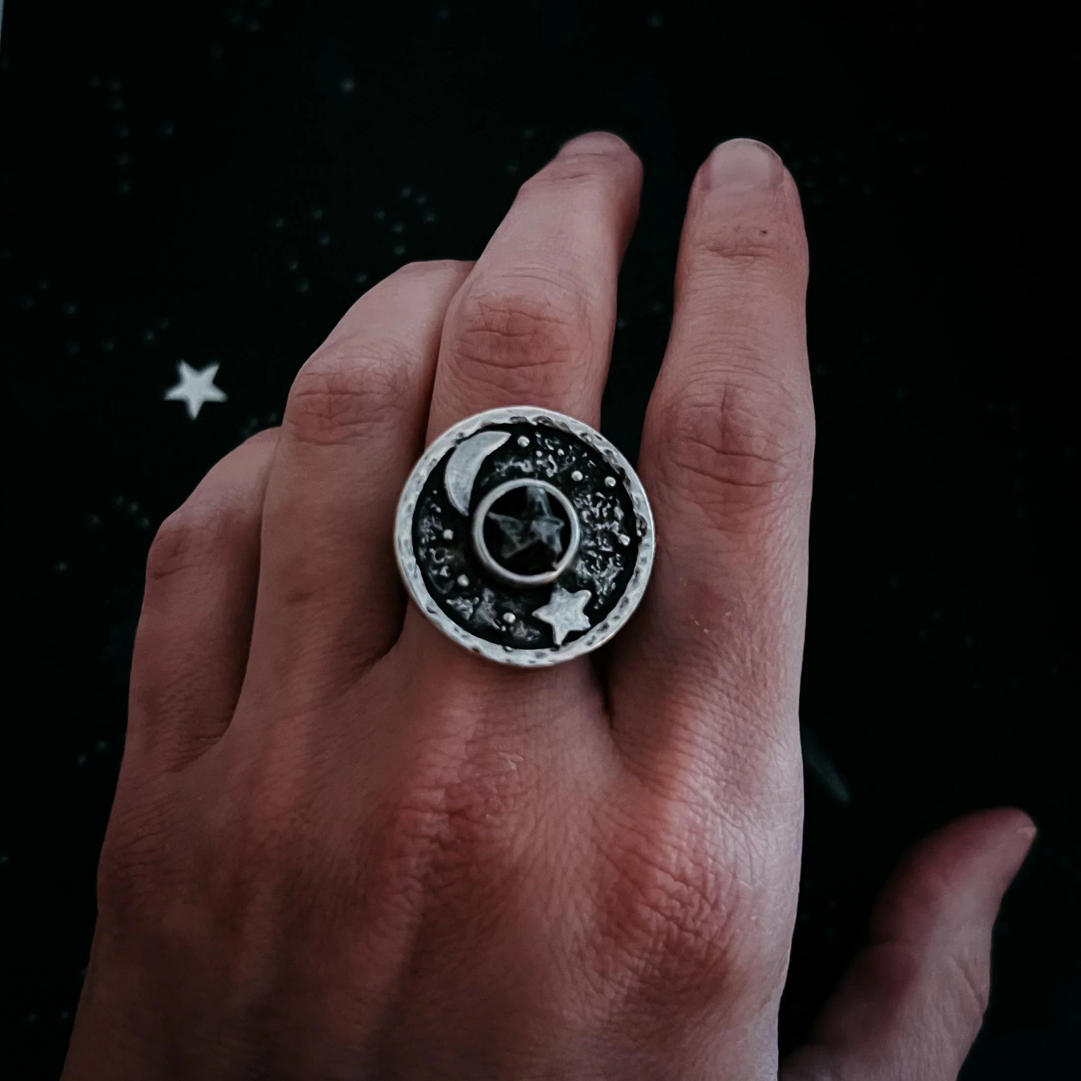 Close-up of hand wearing silver ring with moon and star design on dark starry background