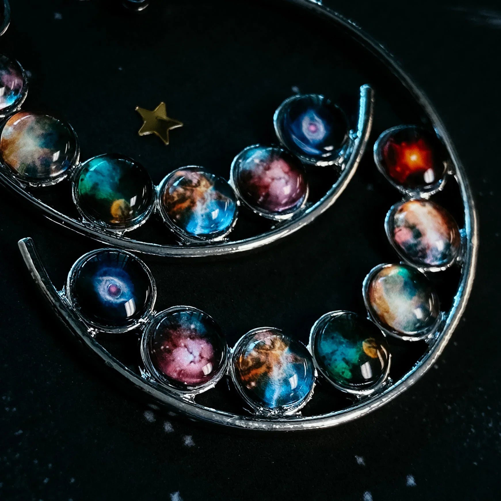 Close-up of curved silver jewelry with colorful galaxy-themed glass beads and a small gold star on black background