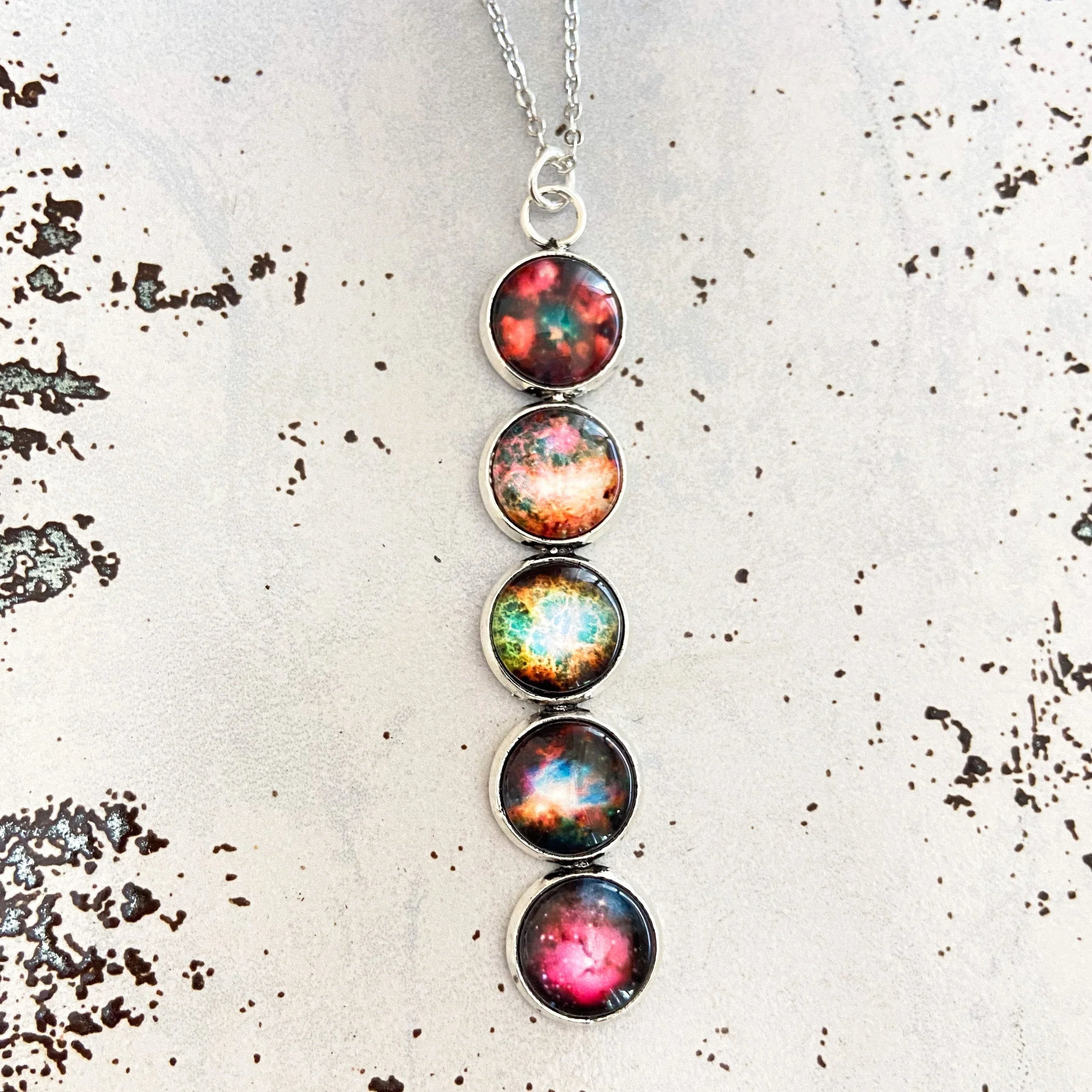 Silver pendant necklace with four round galaxy-themed colorful cabochons on textured white surface