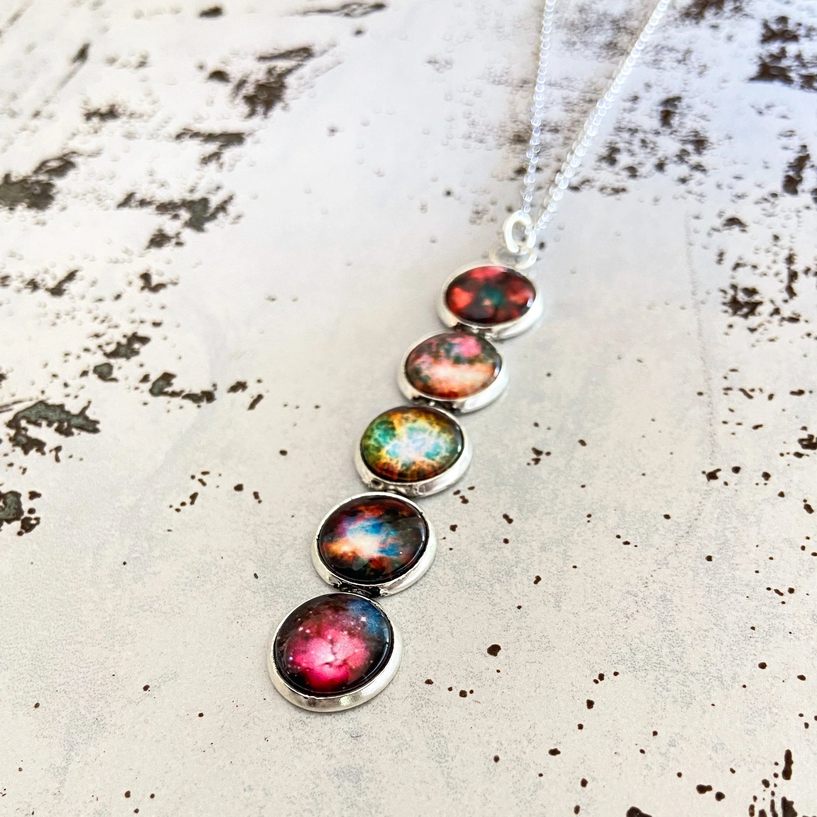 Silver necklace pendant with five round colorful galaxy-themed cabochons on textured white surface