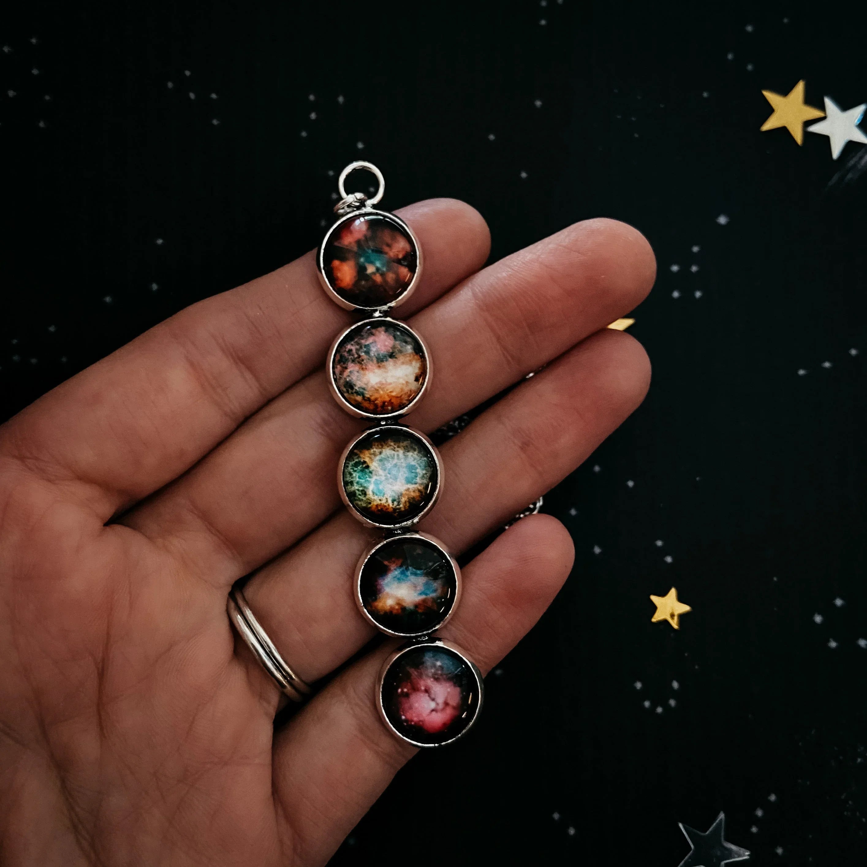 Hand holding a cosmic galaxy-themed pendant with five round colorful nebula designs on a starry background