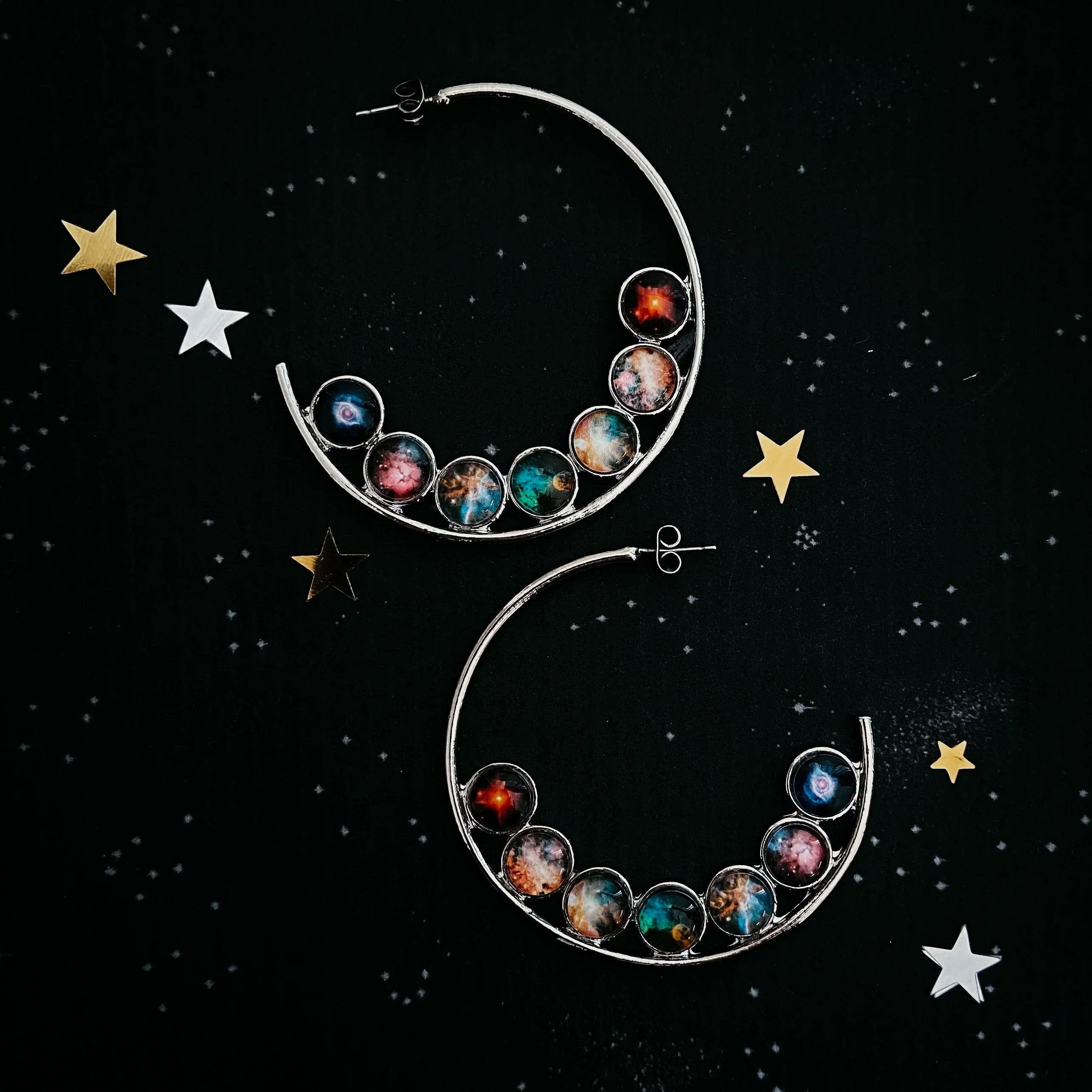 Silver crescent hoop earrings with colorful galaxy planet designs on black starry background