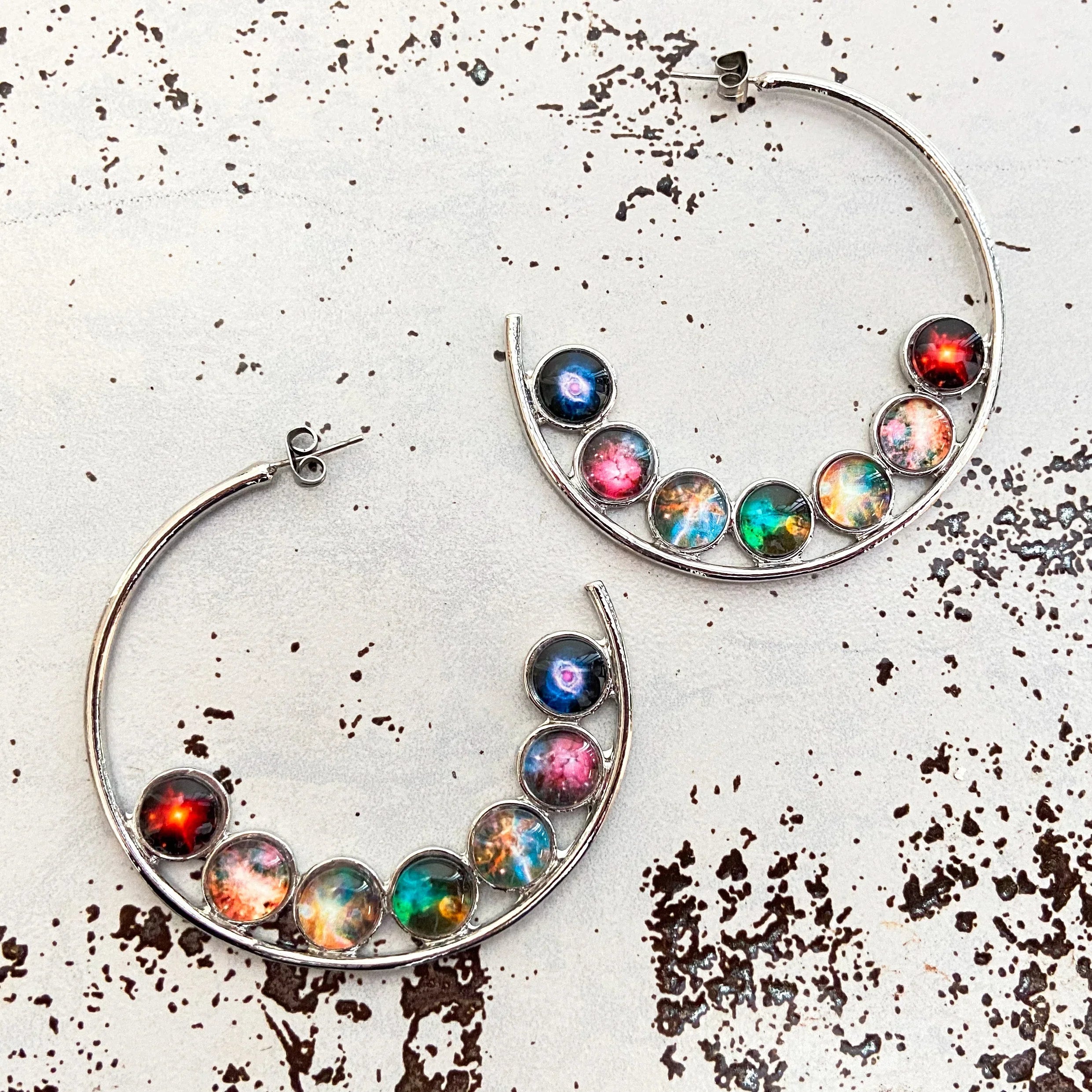 Silver hoop earrings with colorful celestial galaxy stone embellishments on distressed white background