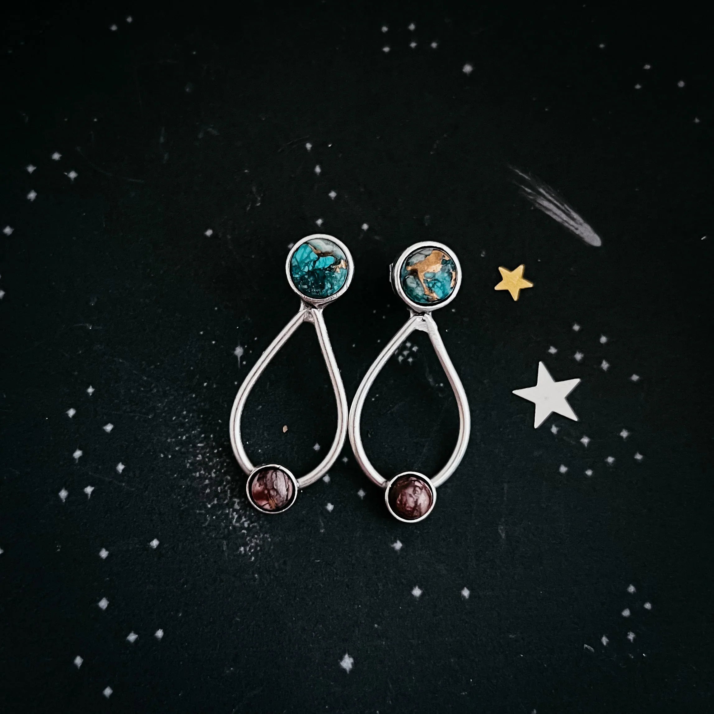 Silver drop-shaped earrings with turquoise and brown stones on starry black background
