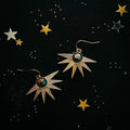 Cosmic starburst gold earrings with gemstone accents on a starry black background at Qu!rk Boutique