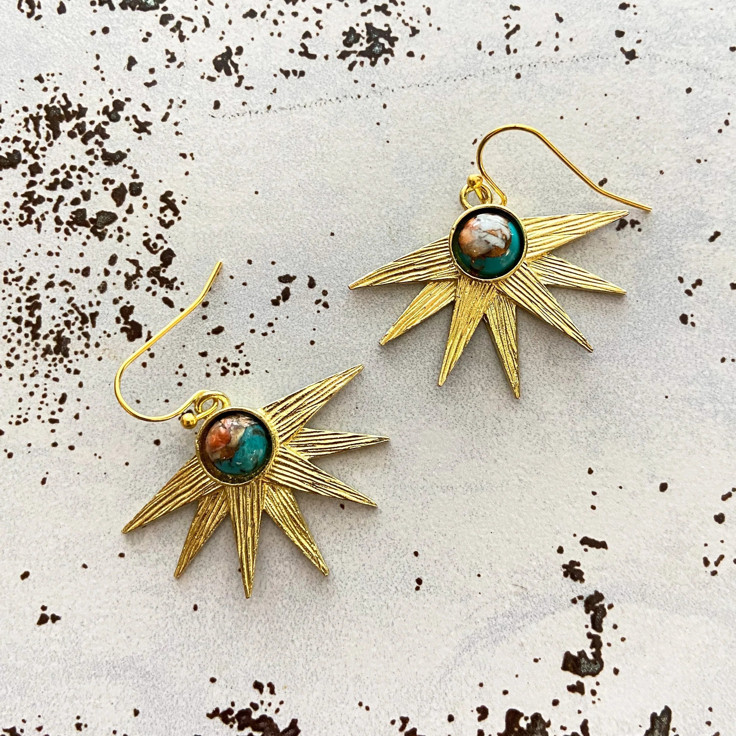 Gold sunburst earrings with turquoise center stones on speckled background, cosmic jewelry