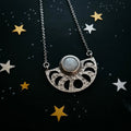 Silver crescent moon necklace with central round gemstone on starry black background