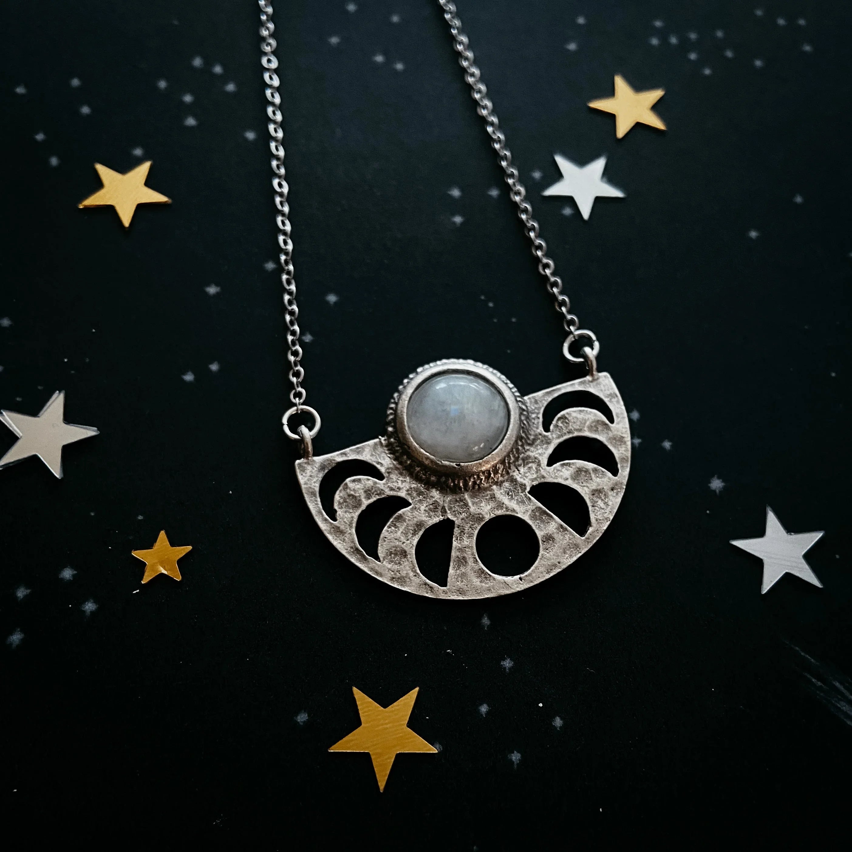 Silver crescent moon necklace with central round gemstone on starry black background