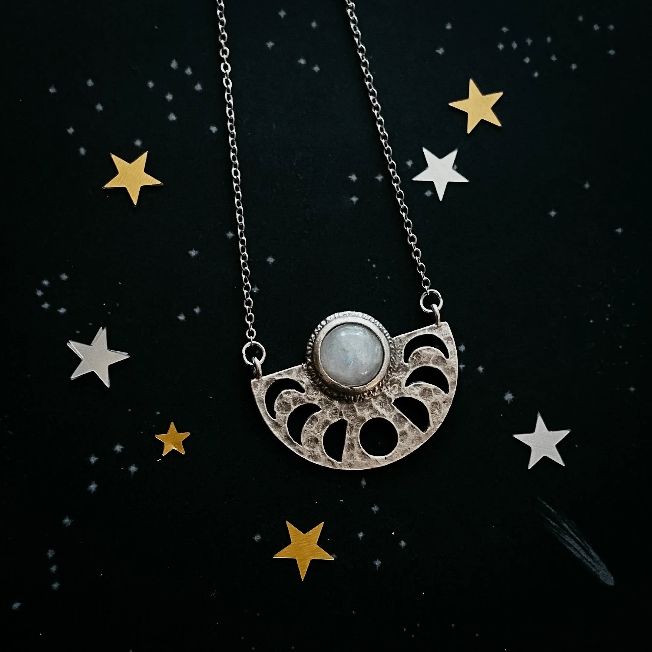 Silver necklace with moon phase cutouts and moonstone pendant on star-patterned black surface
