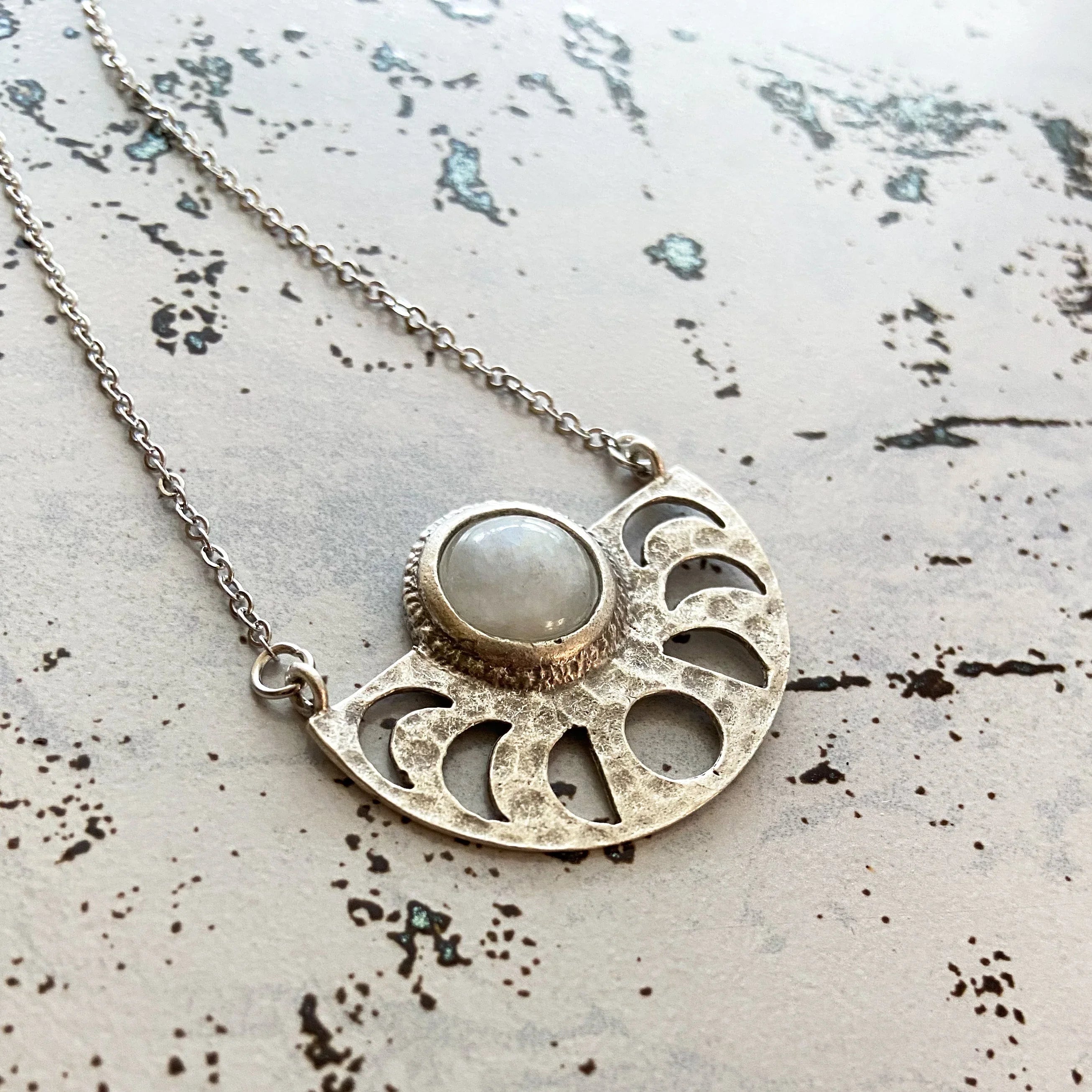 Silver necklace with crescent moon cutouts and central round moonstone pendant on textured surface