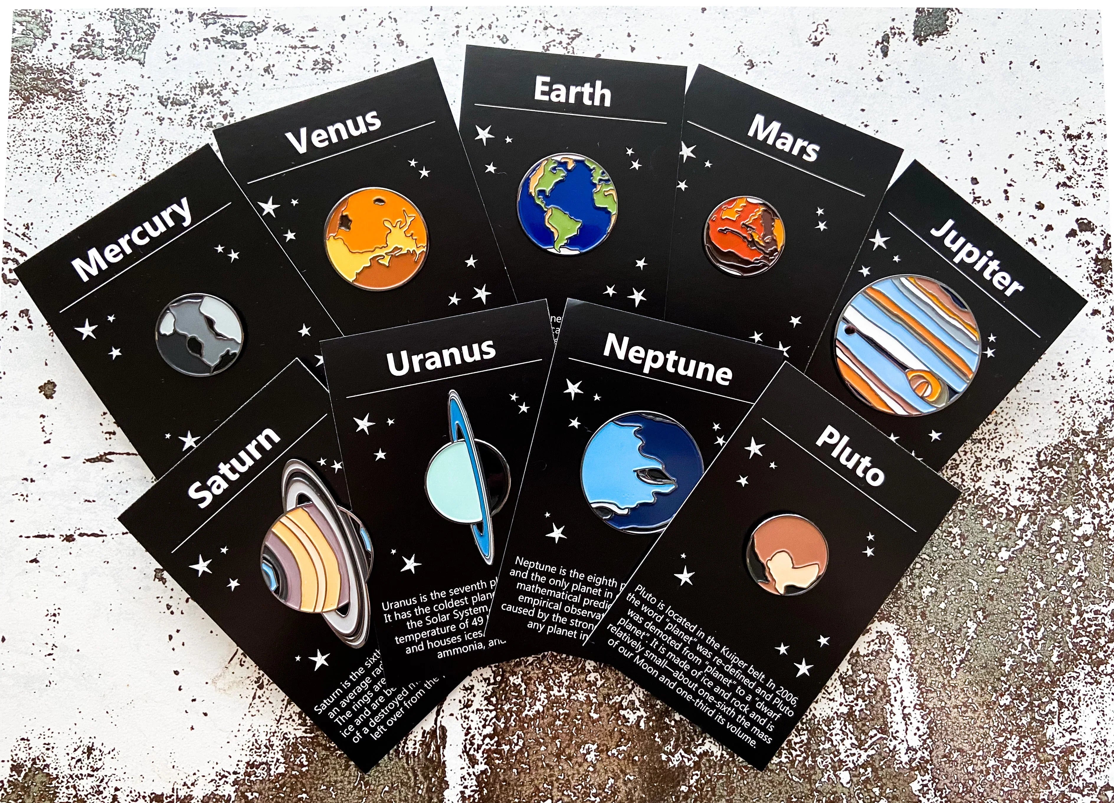 Set of nine colorful enamel planet pins on black cards labeled Mercury, Venus, Earth, Mars, Jupiter, Saturn, Uranus, Neptune, and Pluto