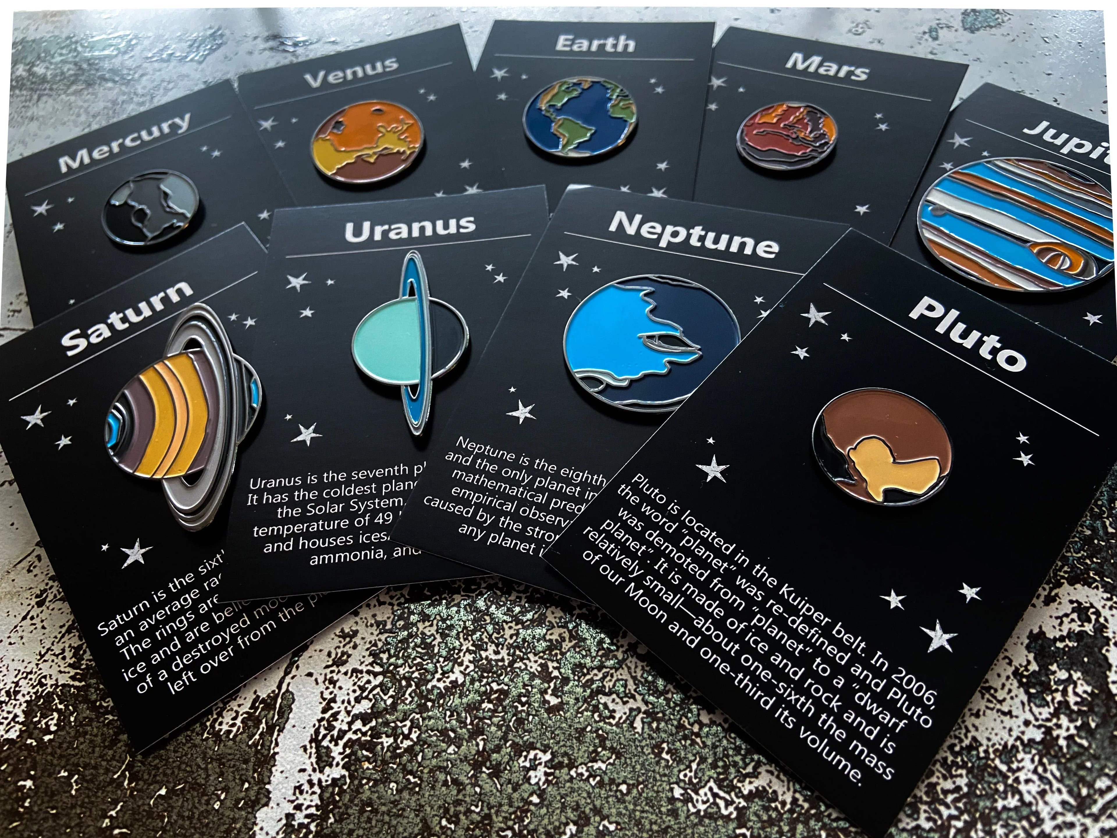 Set of enamel pins depicting planets of the solar system with black informational cards and star background