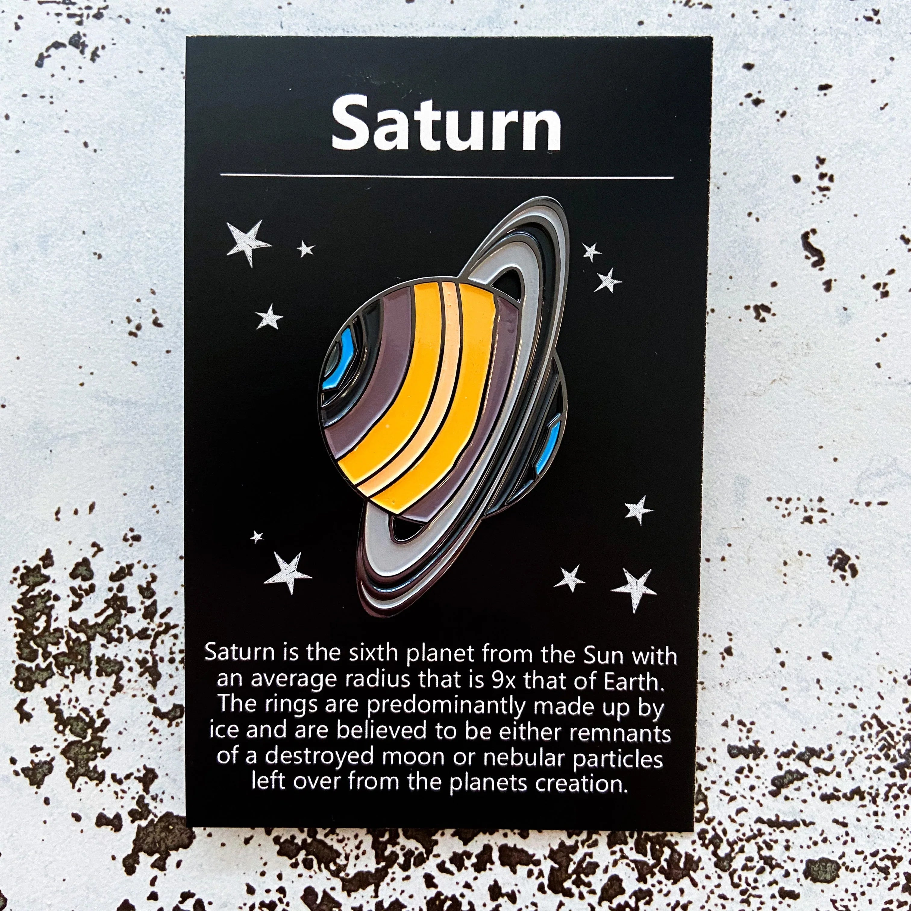 Saturn enamel pin on black starry card, artist-designed gift at Qu!rk Boutique