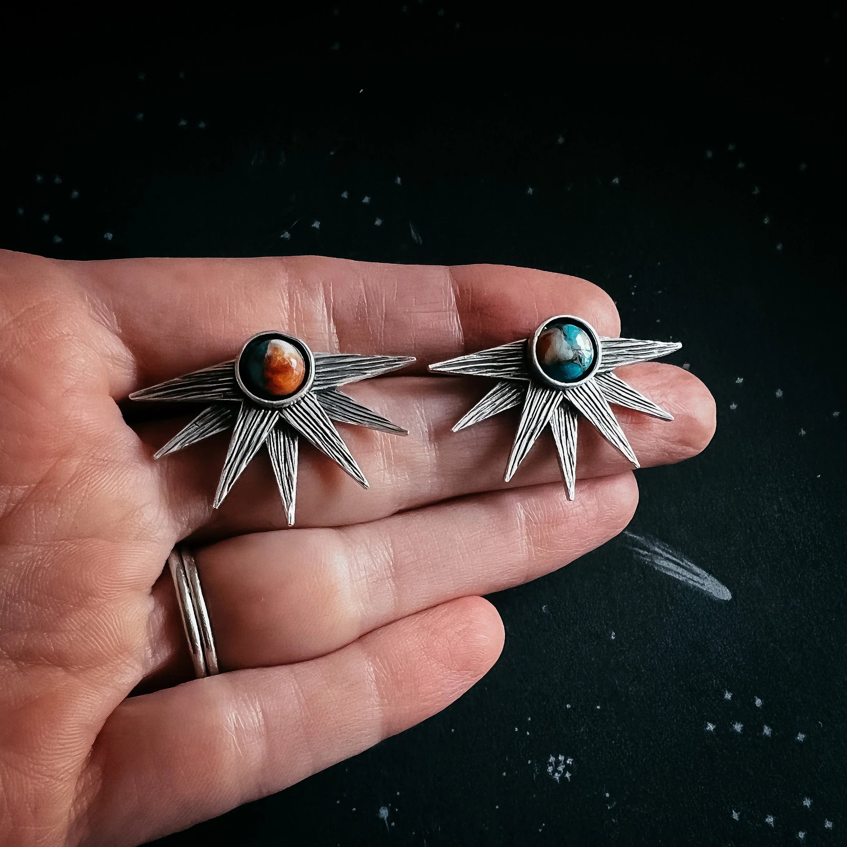 Hand holding cosmic-inspired silver starburst earrings with colorful stone centers, Qu!rk Boutique